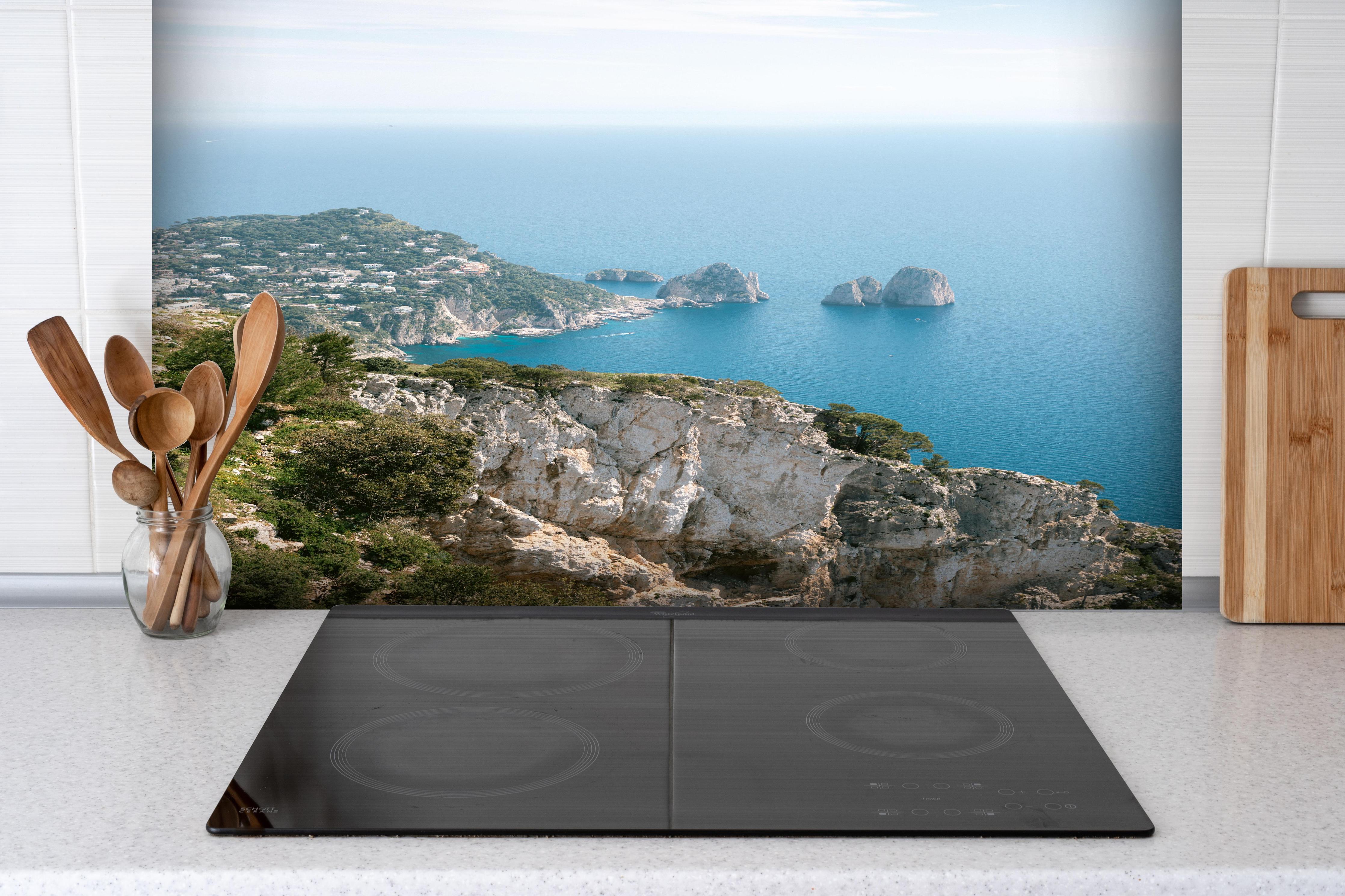 Spritzschutz - Idyllische Capri Küste und blaues Meer hinter einem Cerankochfeld zwischen Holz-Kochutensilien