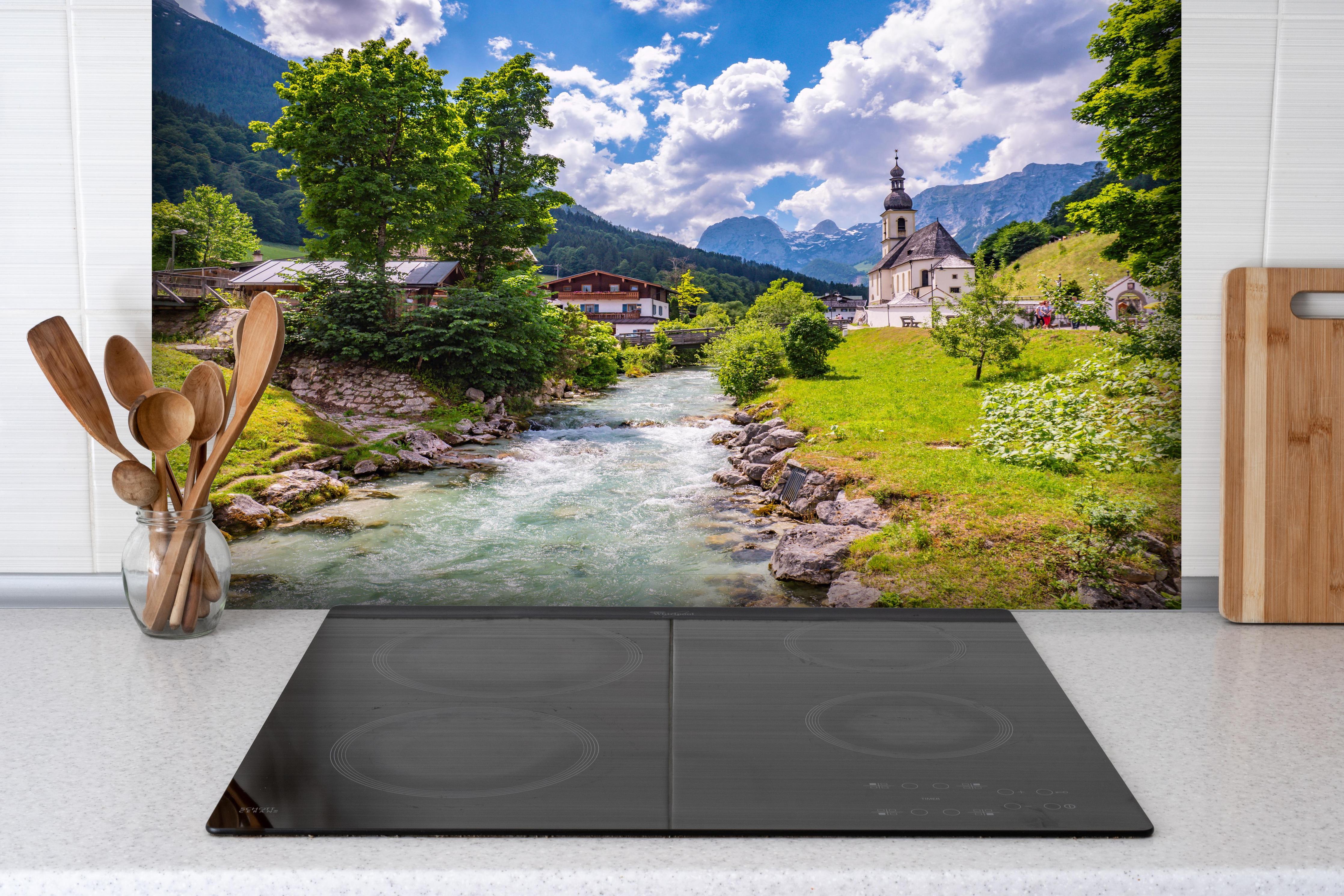Spritzschutz - Idyllische Ramsau Kirche mit Bergblick hinter einem Cerankochfeld zwischen Holz-Kochutensilien