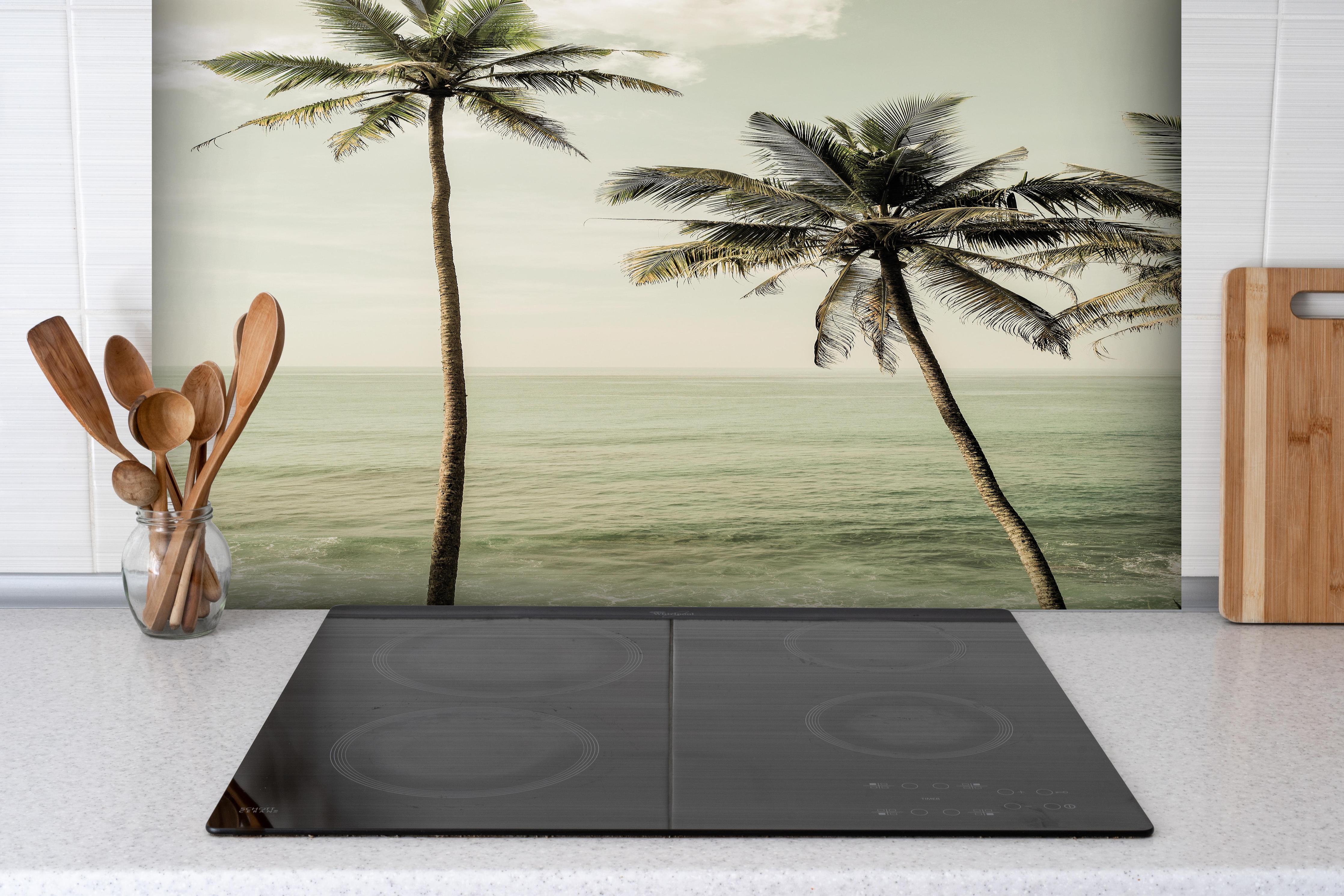 Spritzschutz - Idyllische Strandpalmen über ruhigem Meer hinter einem Cerankochfeld zwischen Holz-Kochutensilien
