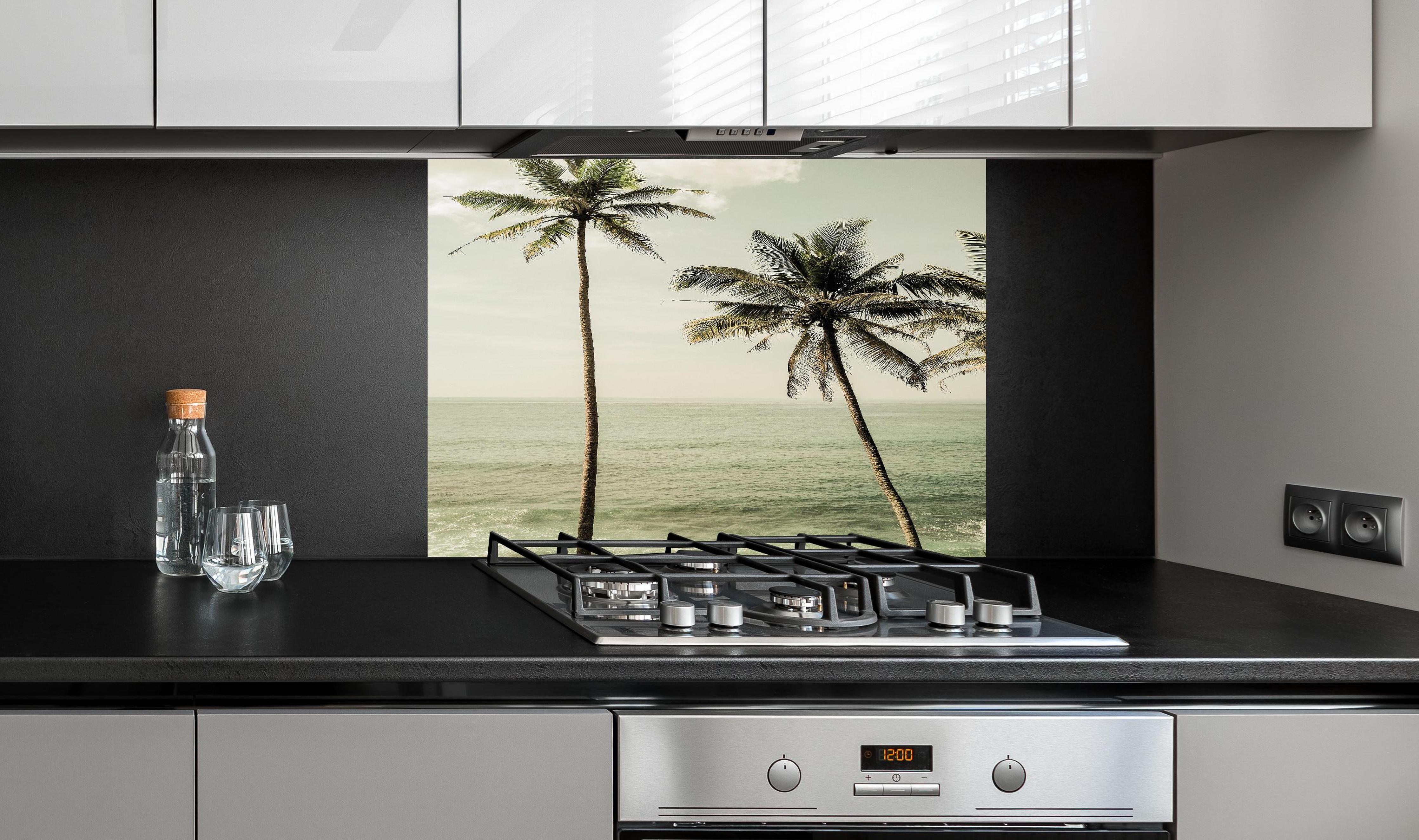 Spritzschutz - Idyllische Strandpalmen über ruhigem Meer hinter einem Cerankochfeld zwischen Holz-Kochutensilien