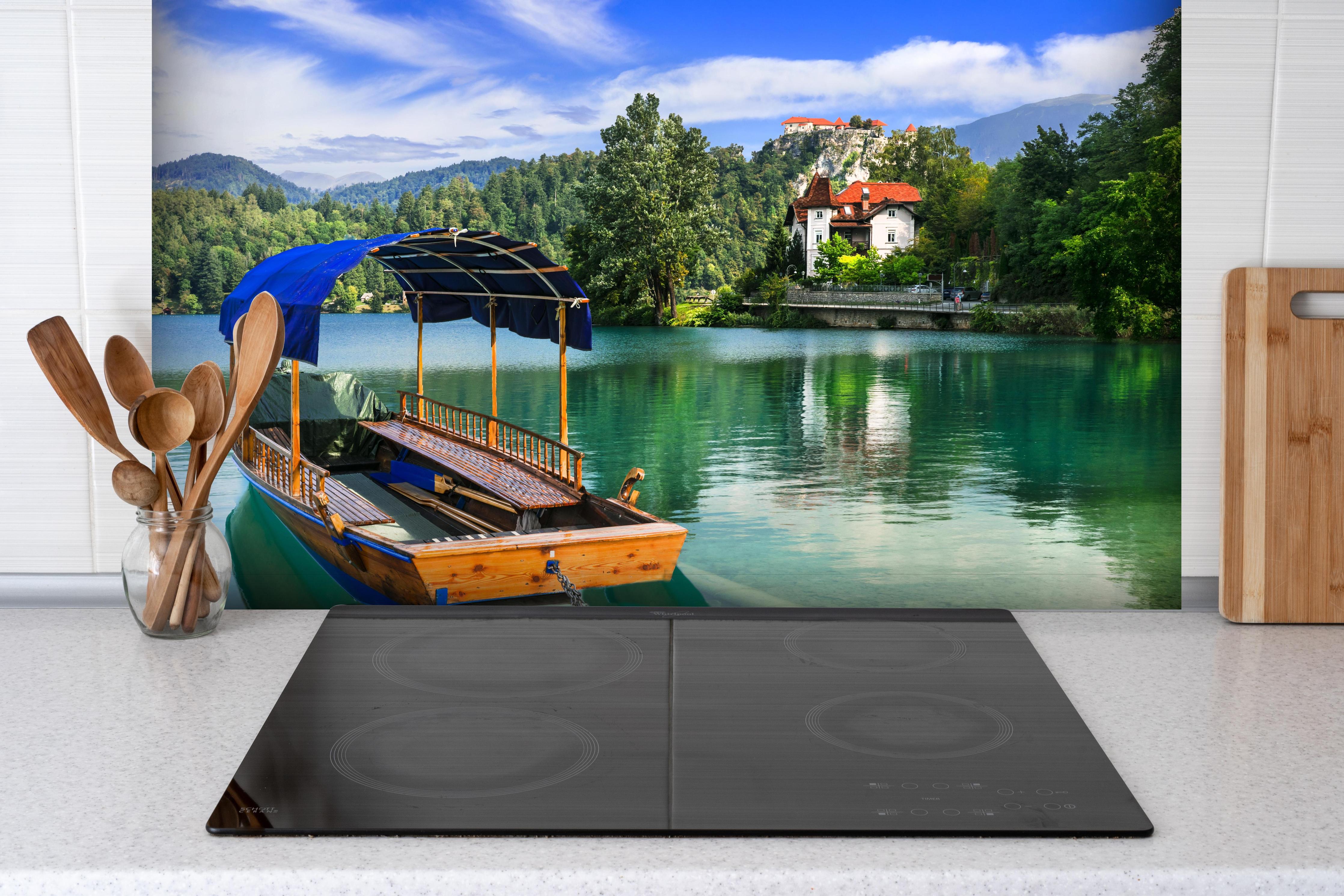 Spritzschutz - Idyllischer Bled See, Holzboot, Slowenien hinter einem Cerankochfeld zwischen Holz-Kochutensilien