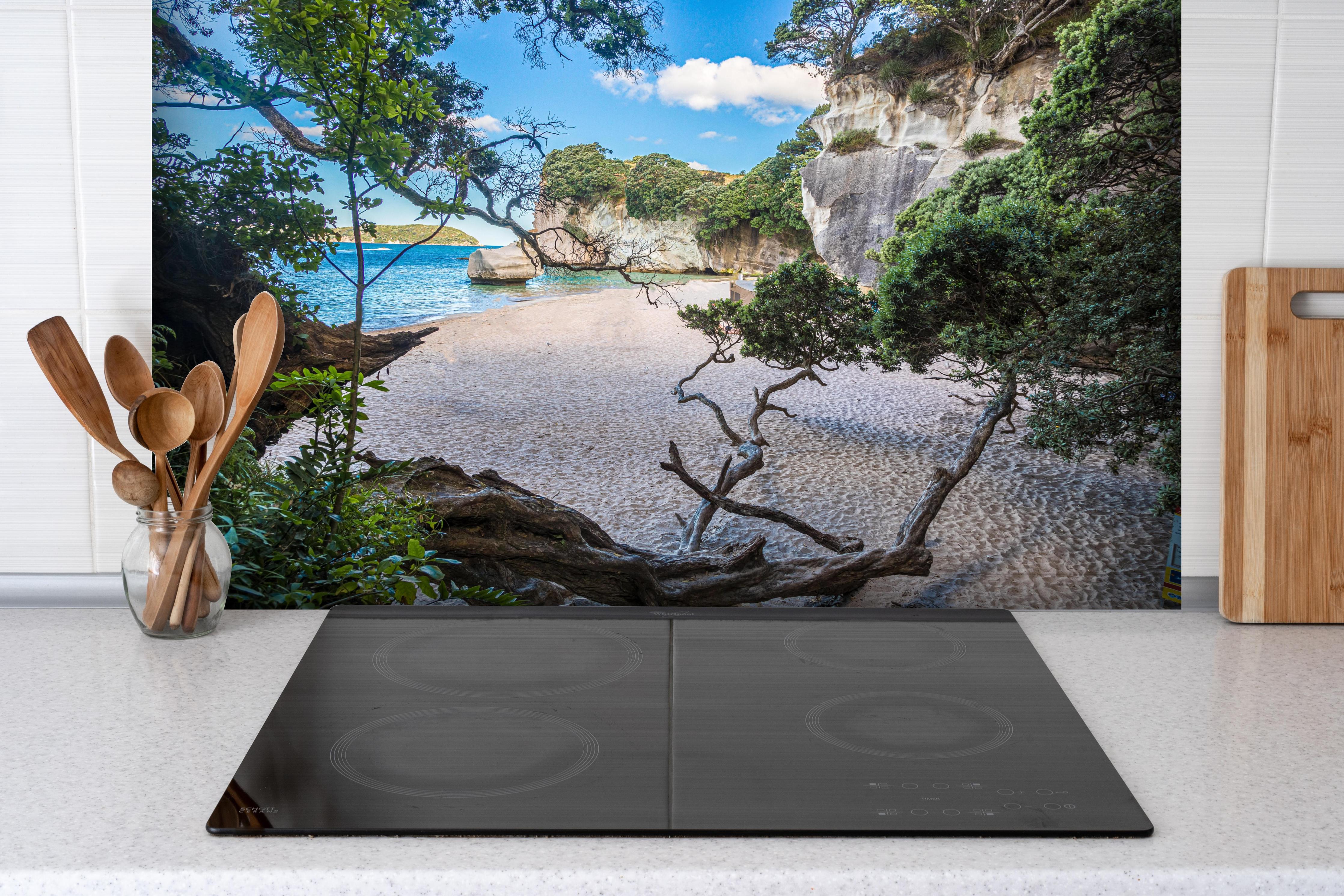 Spritzschutz - Idyllischer Sommerstrand Cathedral Cove hinter einem Cerankochfeld zwischen Holz-Kochutensilien