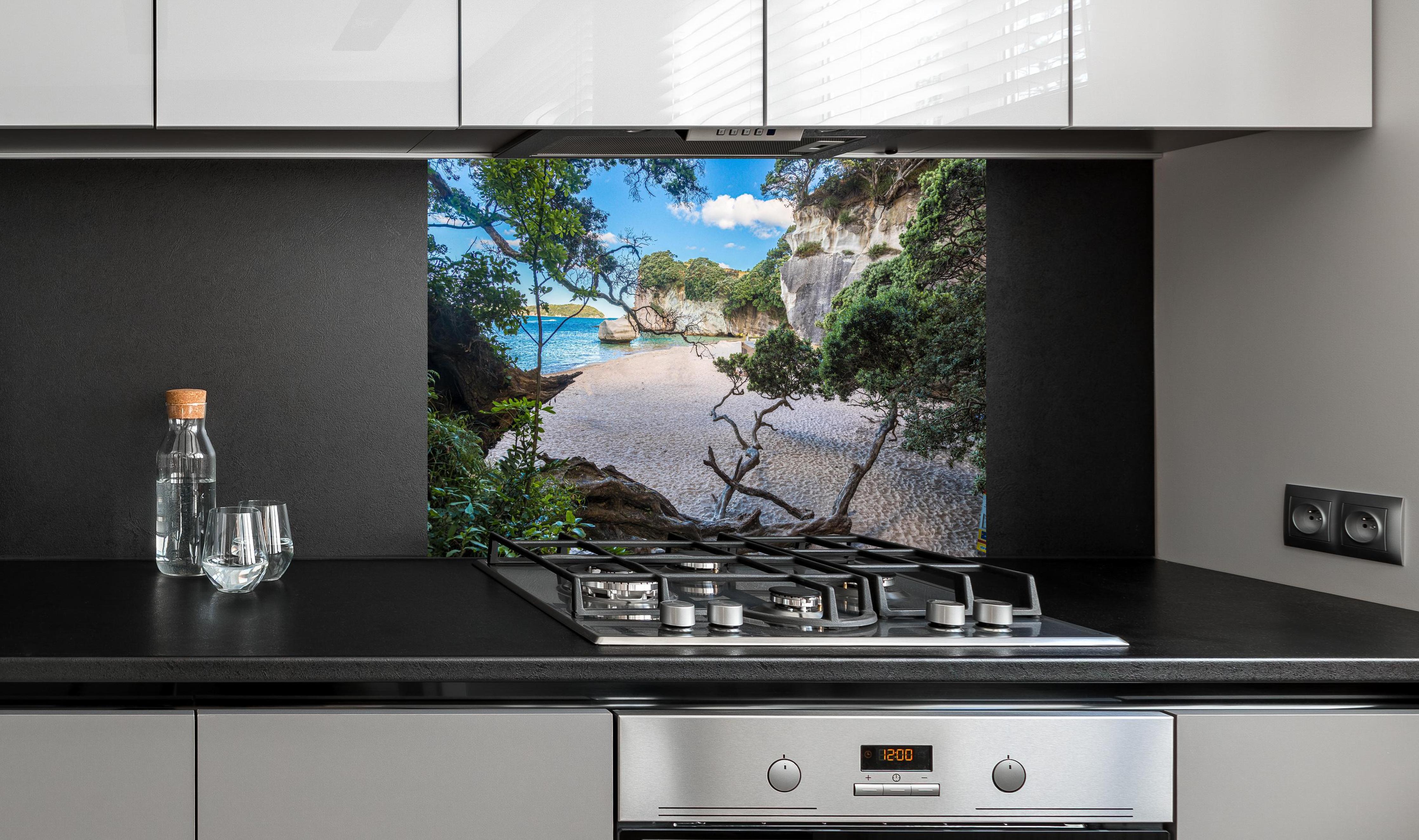 Spritzschutz - Idyllischer Sommerstrand Cathedral Cove hinter einem Cerankochfeld zwischen Holz-Kochutensilien