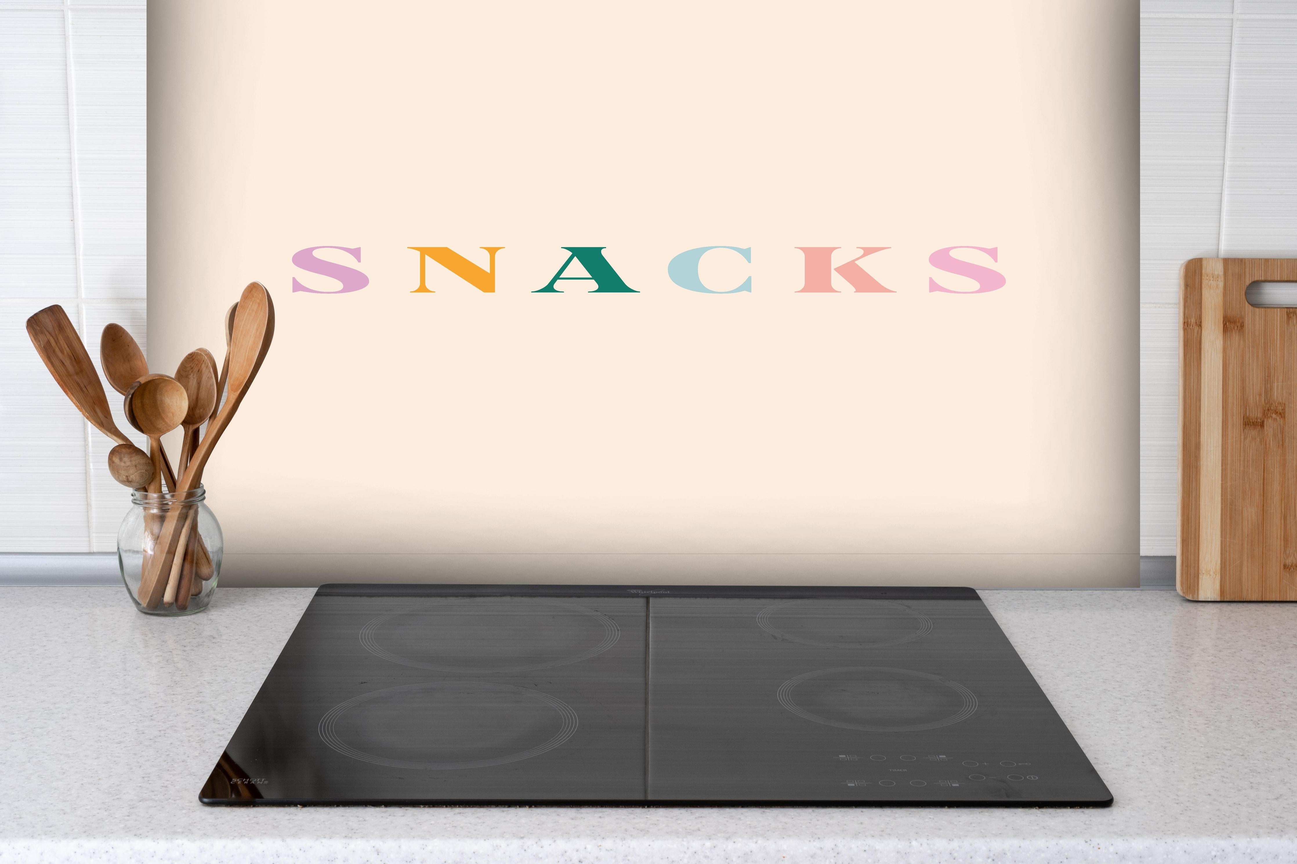 Spritzschutz - Inspirierende 'SNACKS'-Schrift in Pastellfarben hinter einem Cerankochfeld zwischen Holz-Kochutensilien