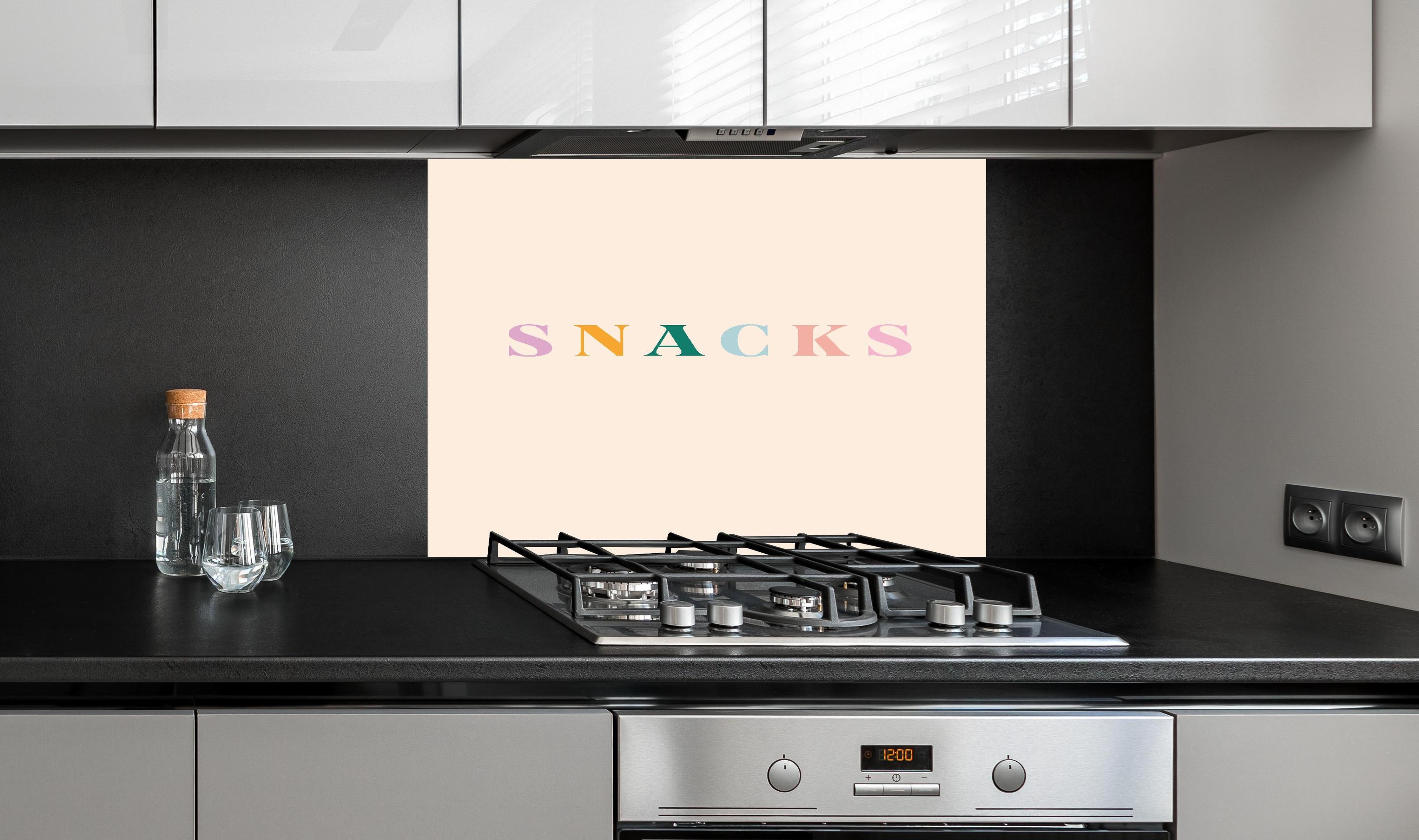 Spritzschutz - Inspirierende 'SNACKS'-Schrift in Pastellfarben hinter einem Cerankochfeld zwischen Holz-Kochutensilien