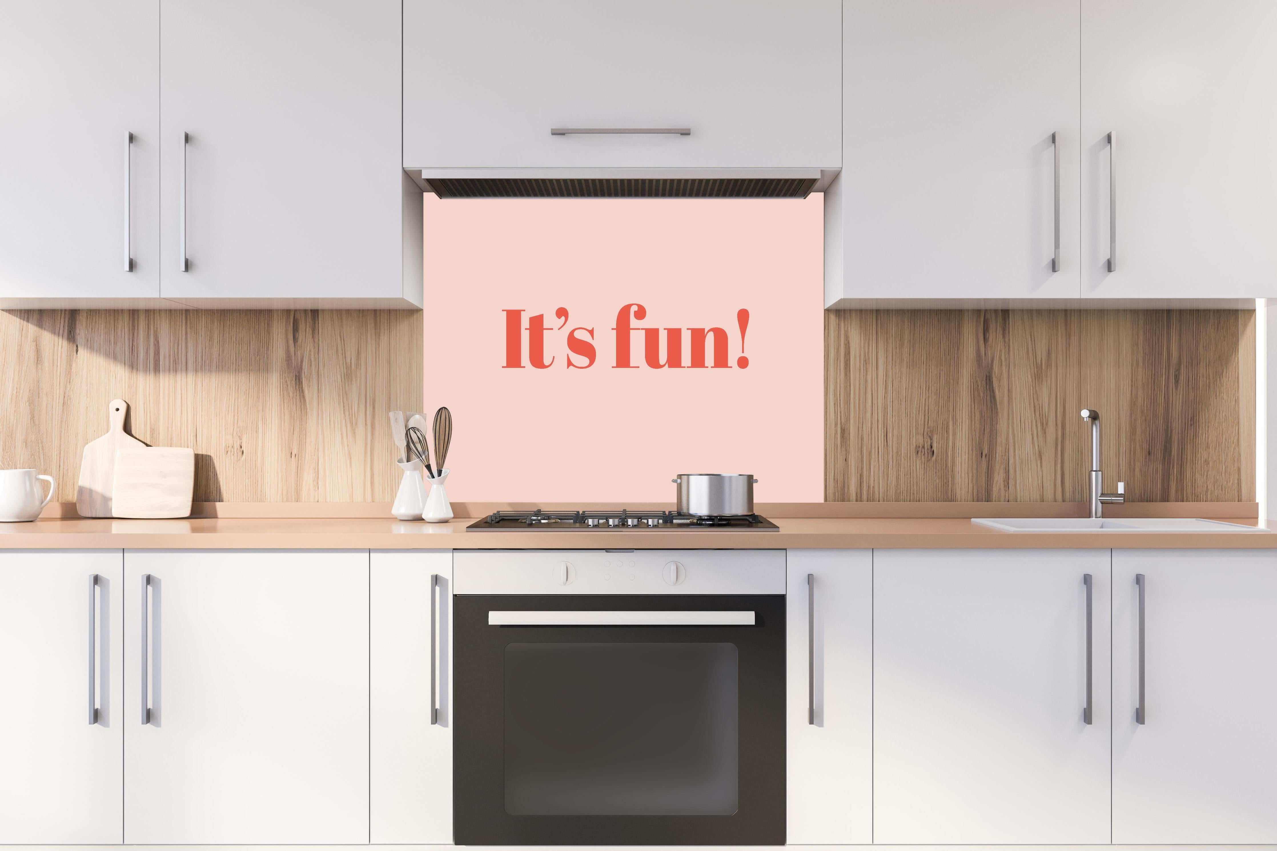 Spritzschutz - Inspirierender 'It's Fun!' Typo-Print in Pink hinter einem Cerankochfeld zwischen Holz-Kochutensilien
