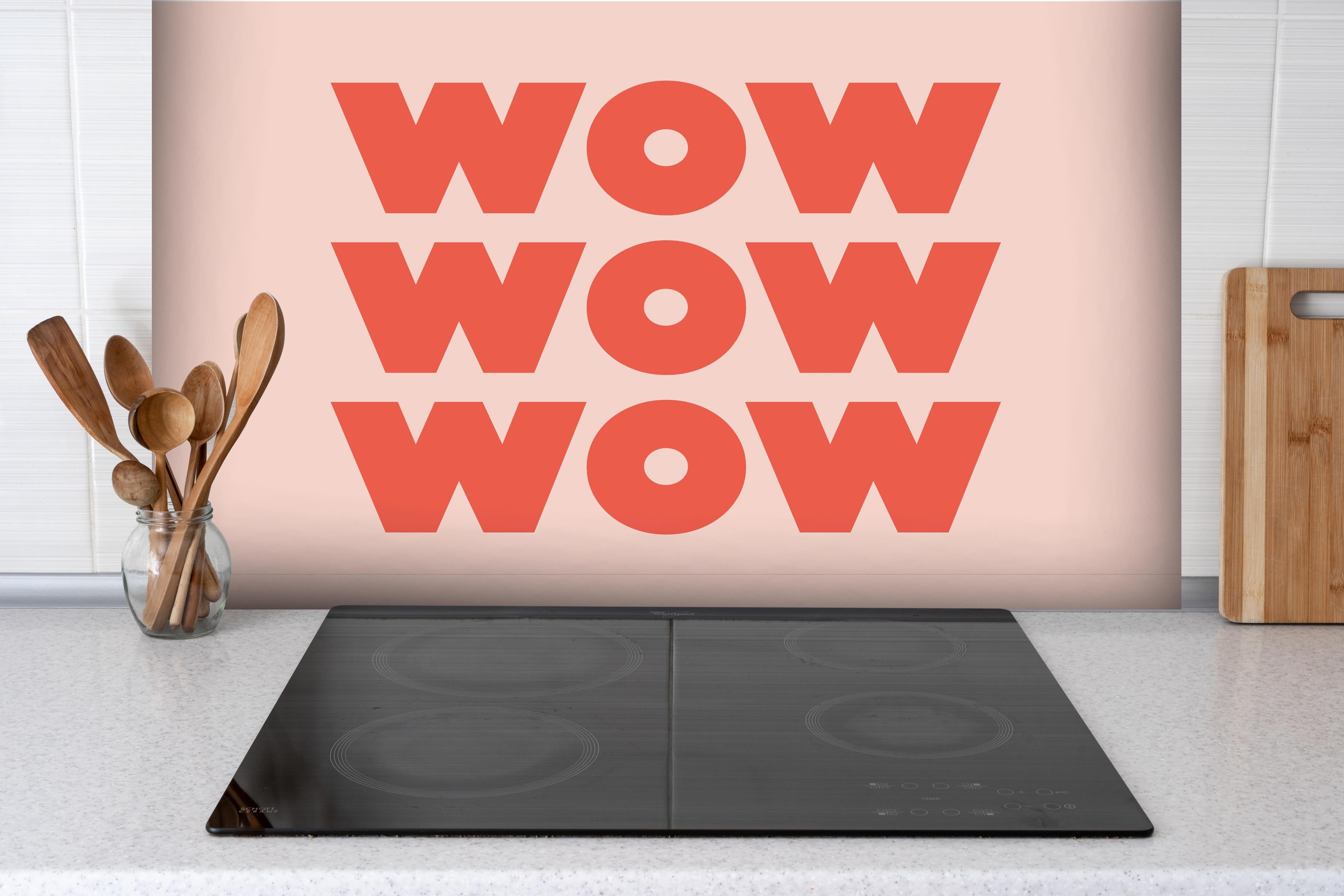 Spritzschutz - Inspirierender 'WOW' Text auf Pinkem Hintergrund hinter einem Cerankochfeld zwischen Holz-Kochutensilien