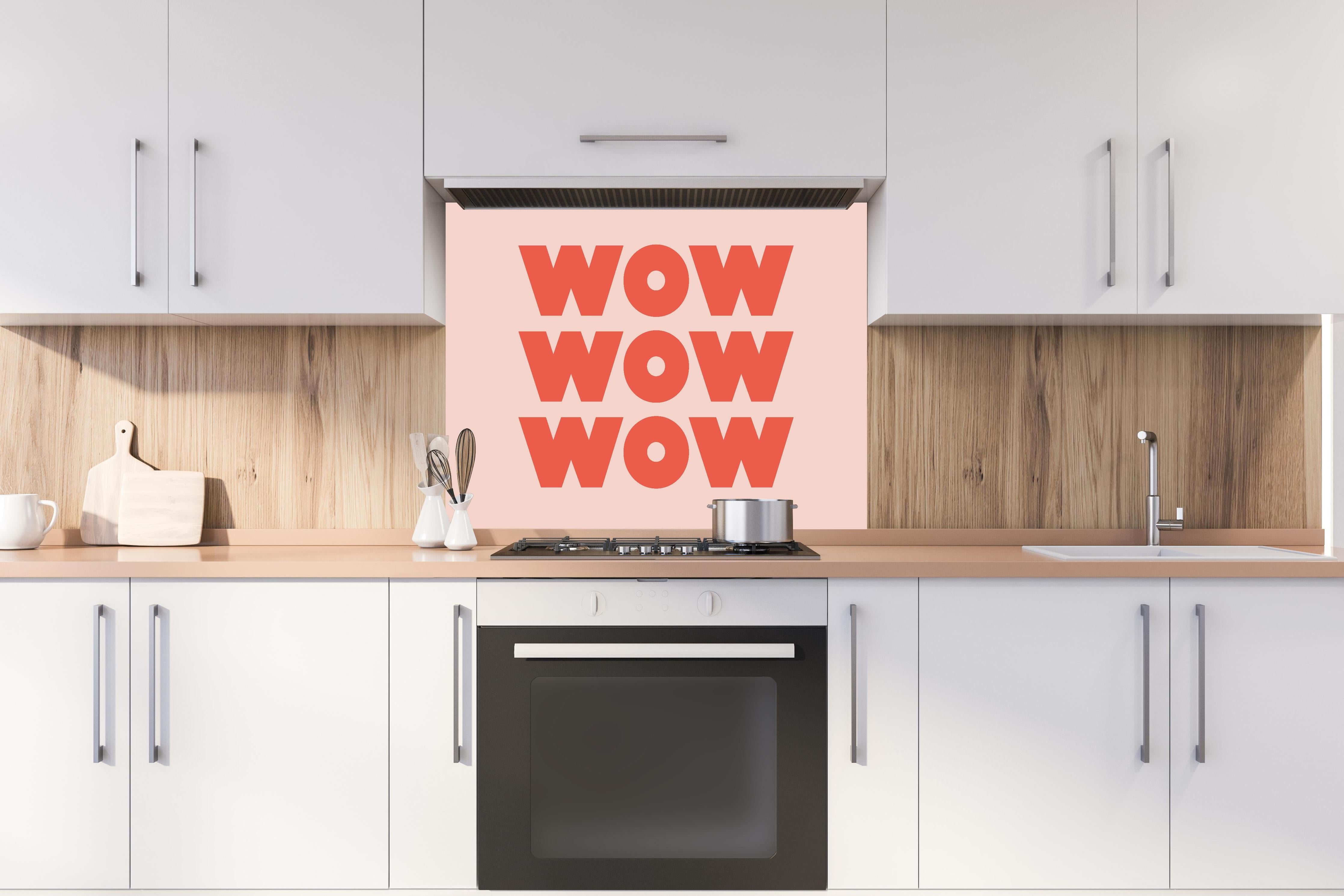 Spritzschutz - Inspirierender 'WOW' Text auf Pinkem Hintergrund hinter einem Cerankochfeld zwischen Holz-Kochutensilien
