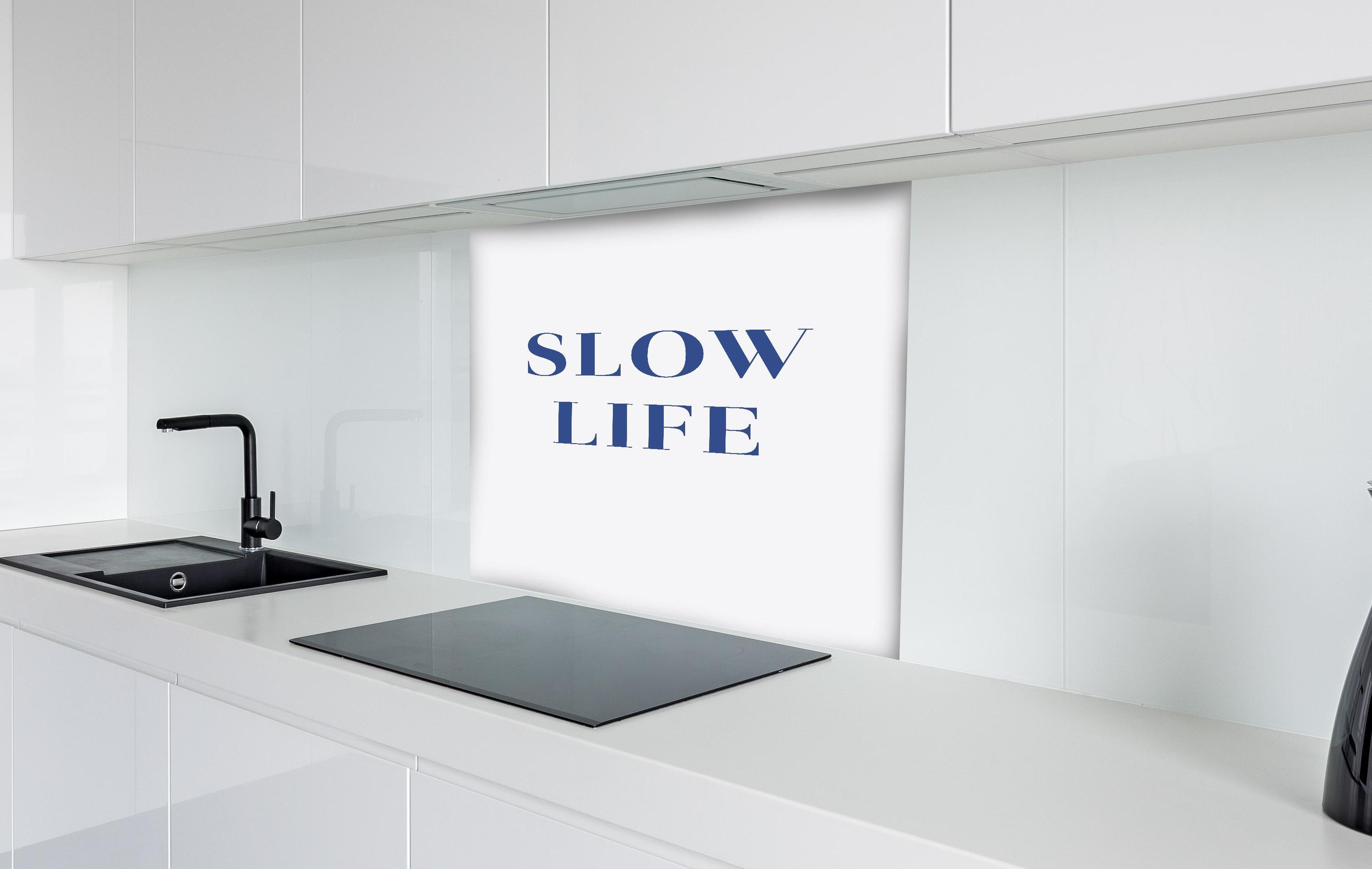 Spritzschutz - Inspirierendes Slow Life Zitat, Blau auf Weiß hinter einem Cerankochfeld zwischen Holz-Kochutensilien