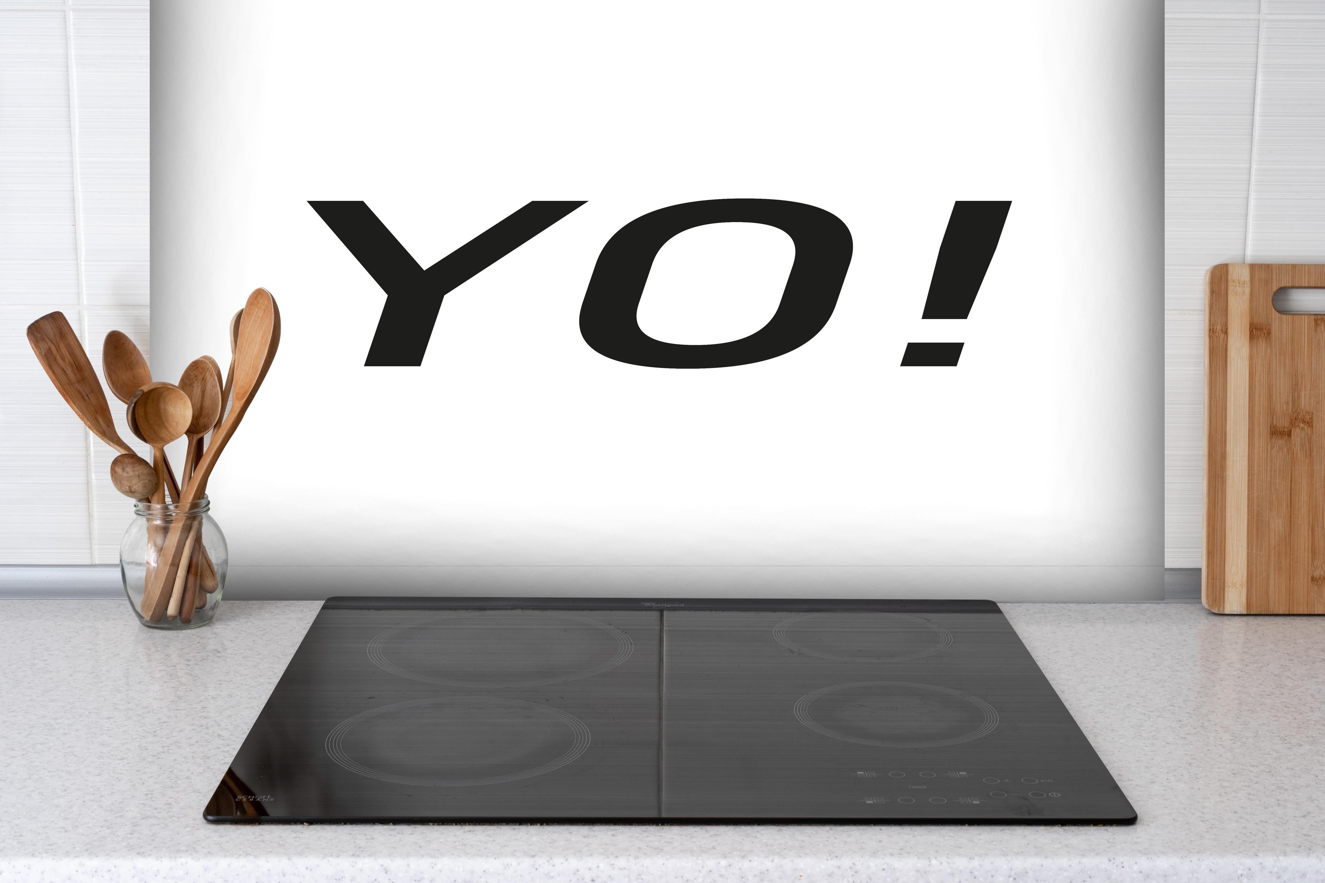 Spritzschutz - Inspirierendes 'YO!' in Schwarz auf Weiß hinter einem Cerankochfeld zwischen Holz-Kochutensilien