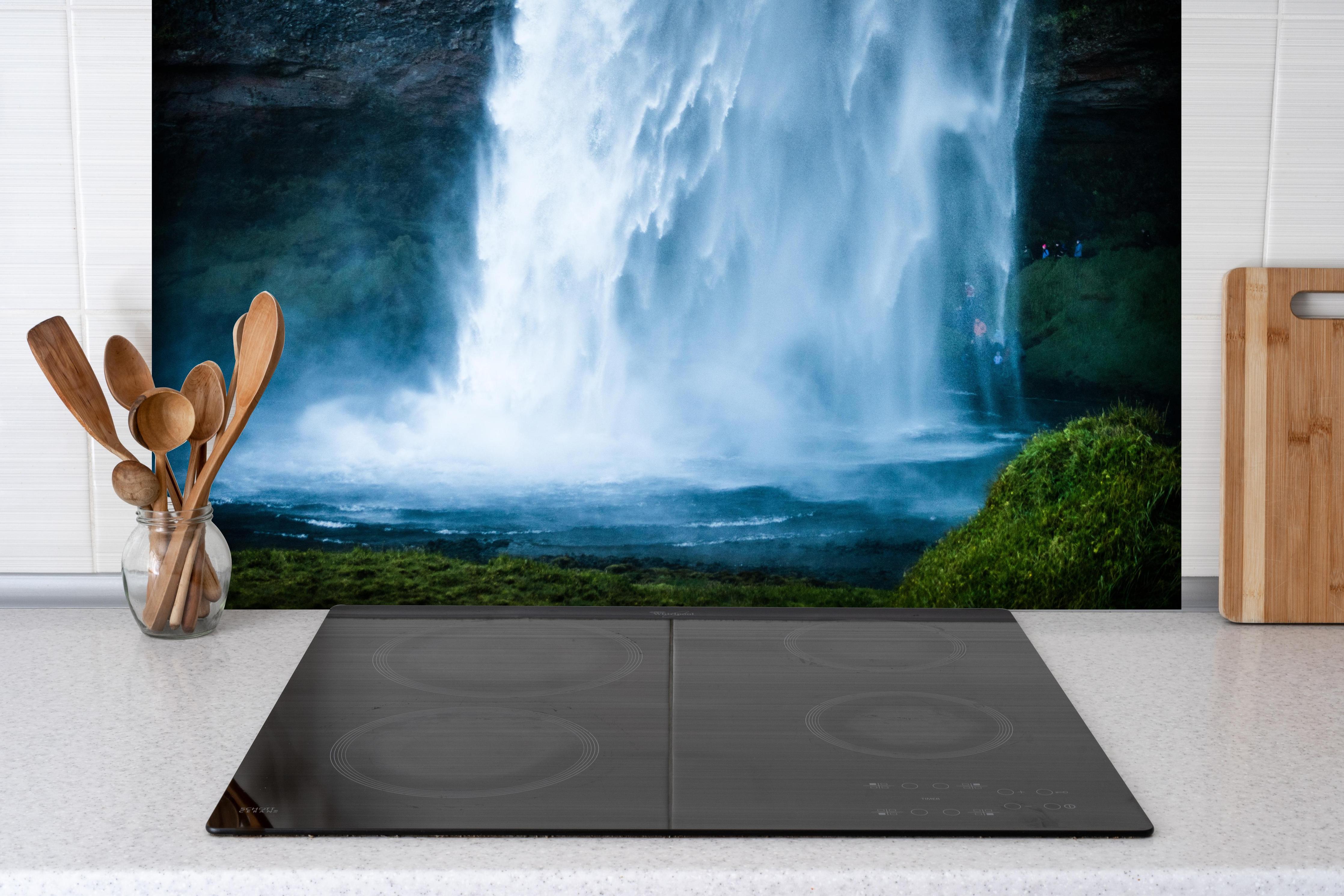 Spritzschutz - Islands beeindruckender Wasserfall in Blau hinter einem Cerankochfeld zwischen Holz-Kochutensilien