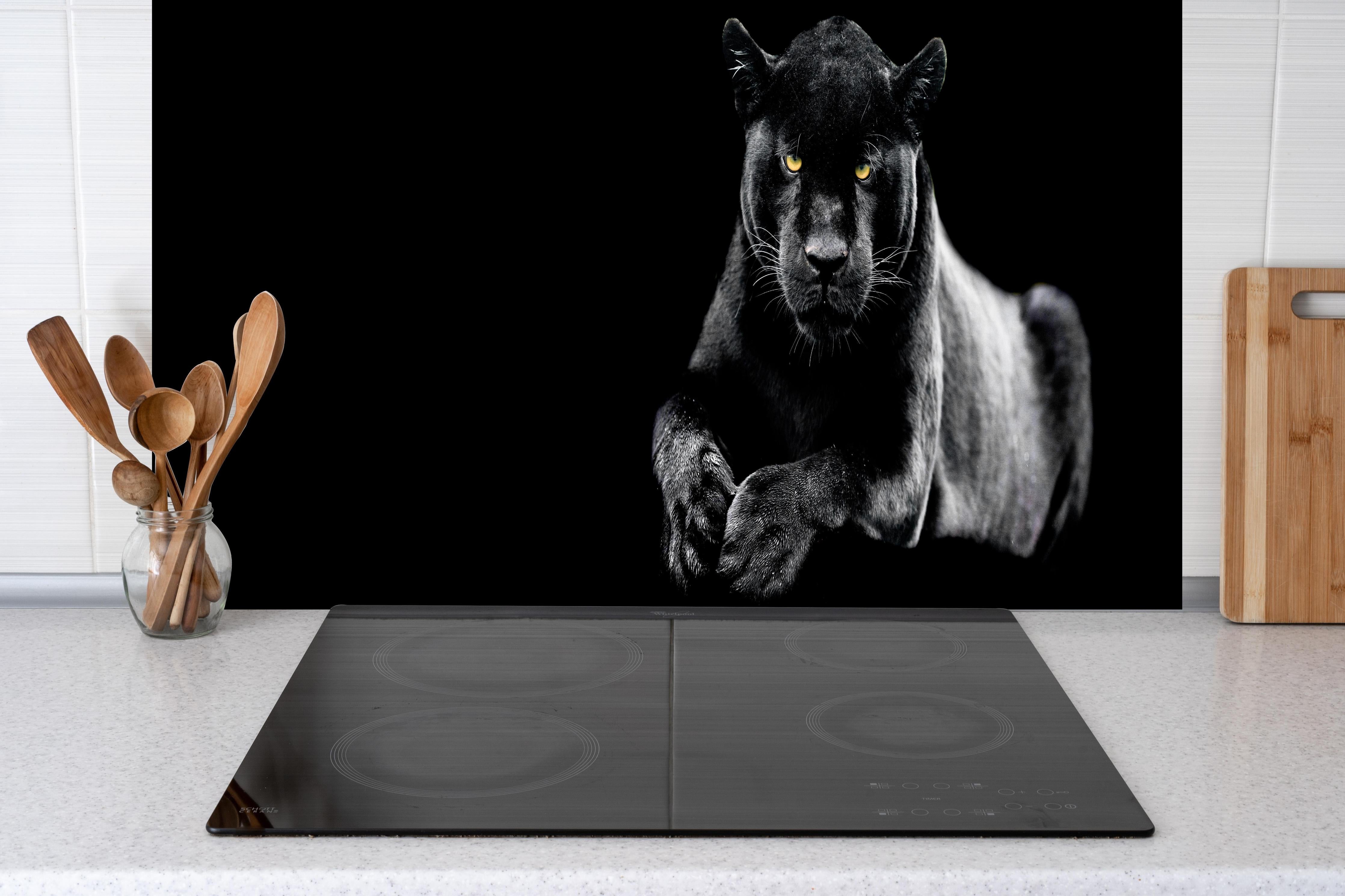 Spritzschutz - Jaguar auf schwarzem Hintergrund hinter einem Cerankochfeld zwischen Holz-Kochutensilien