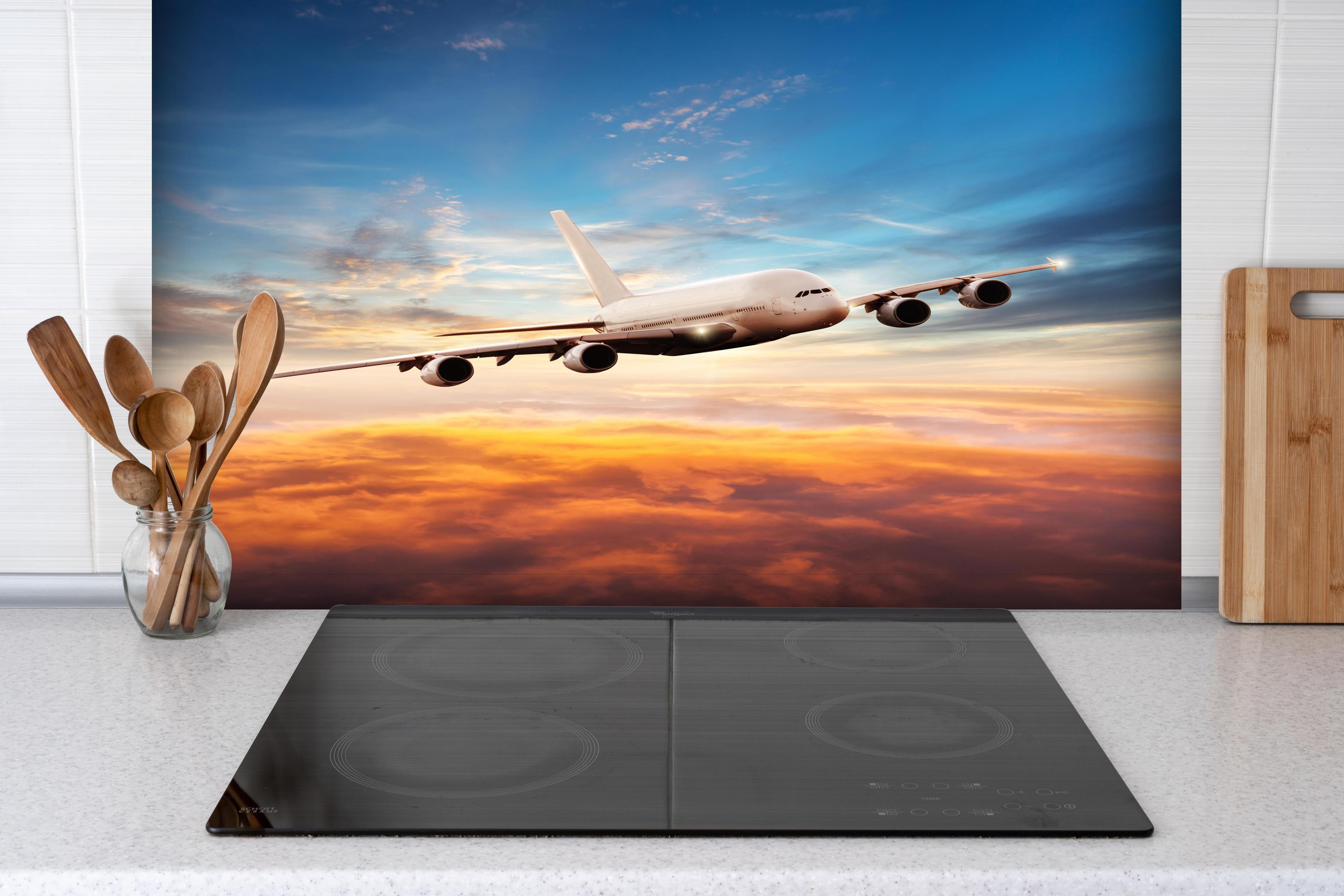 Spritzschutz - Jet im Sonnenuntergang über Wolken hinter einem Cerankochfeld zwischen Holz-Kochutensilien