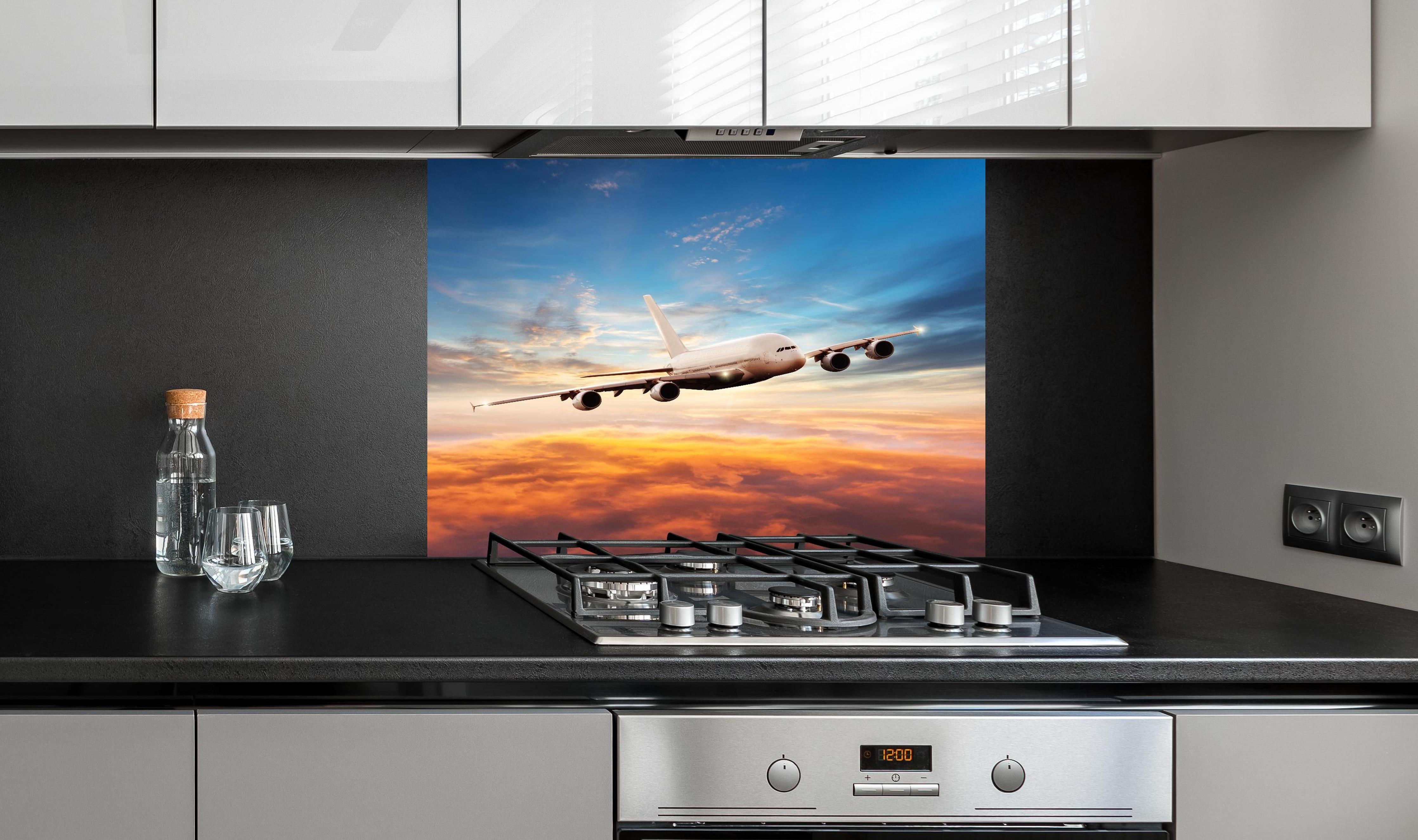 Spritzschutz - Jet im Sonnenuntergang über Wolken hinter einem Cerankochfeld zwischen Holz-Kochutensilien