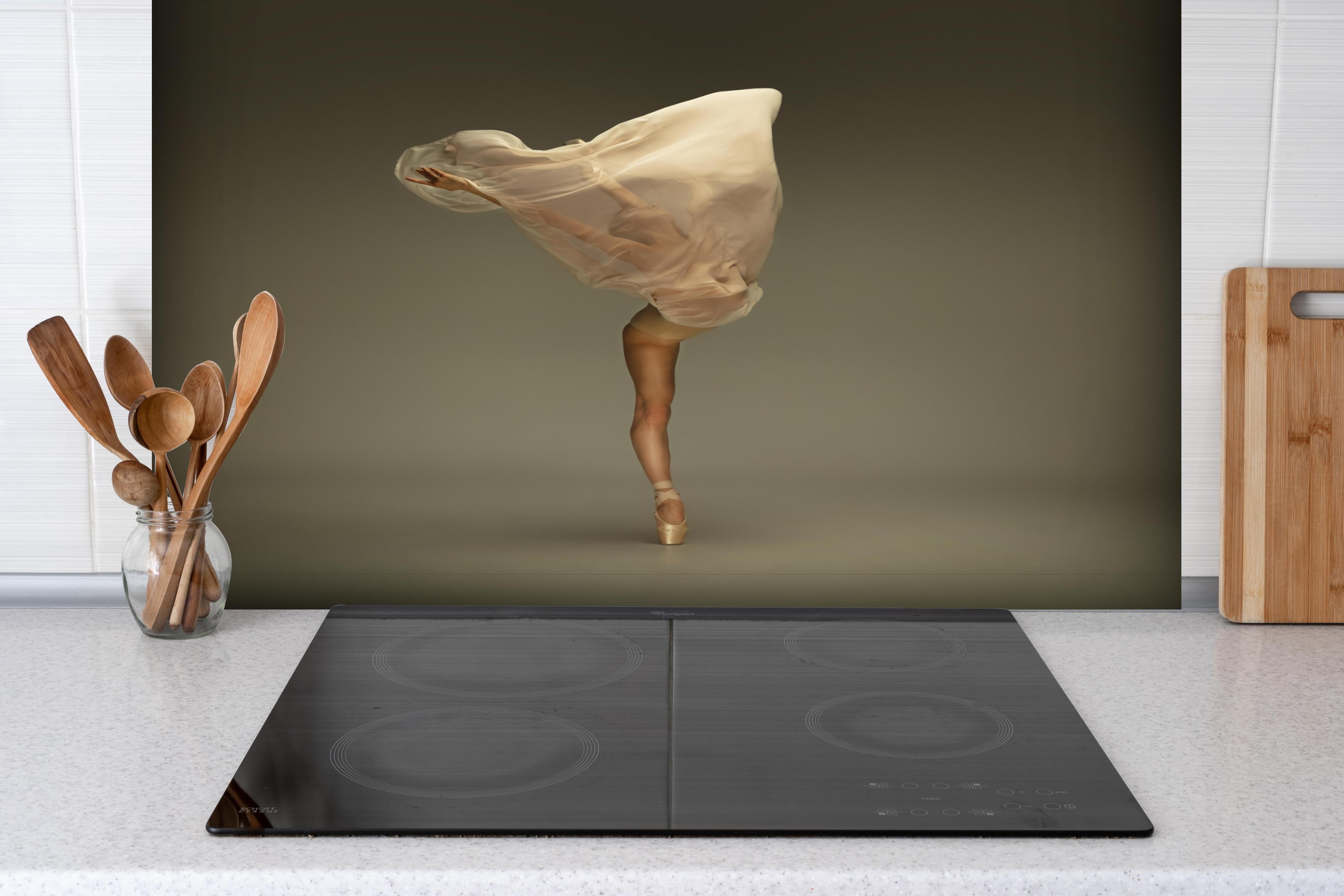 Spritzschutz - Junge Ballerina in grauem Studio hinter einem Cerankochfeld zwischen Holz-Kochutensilien