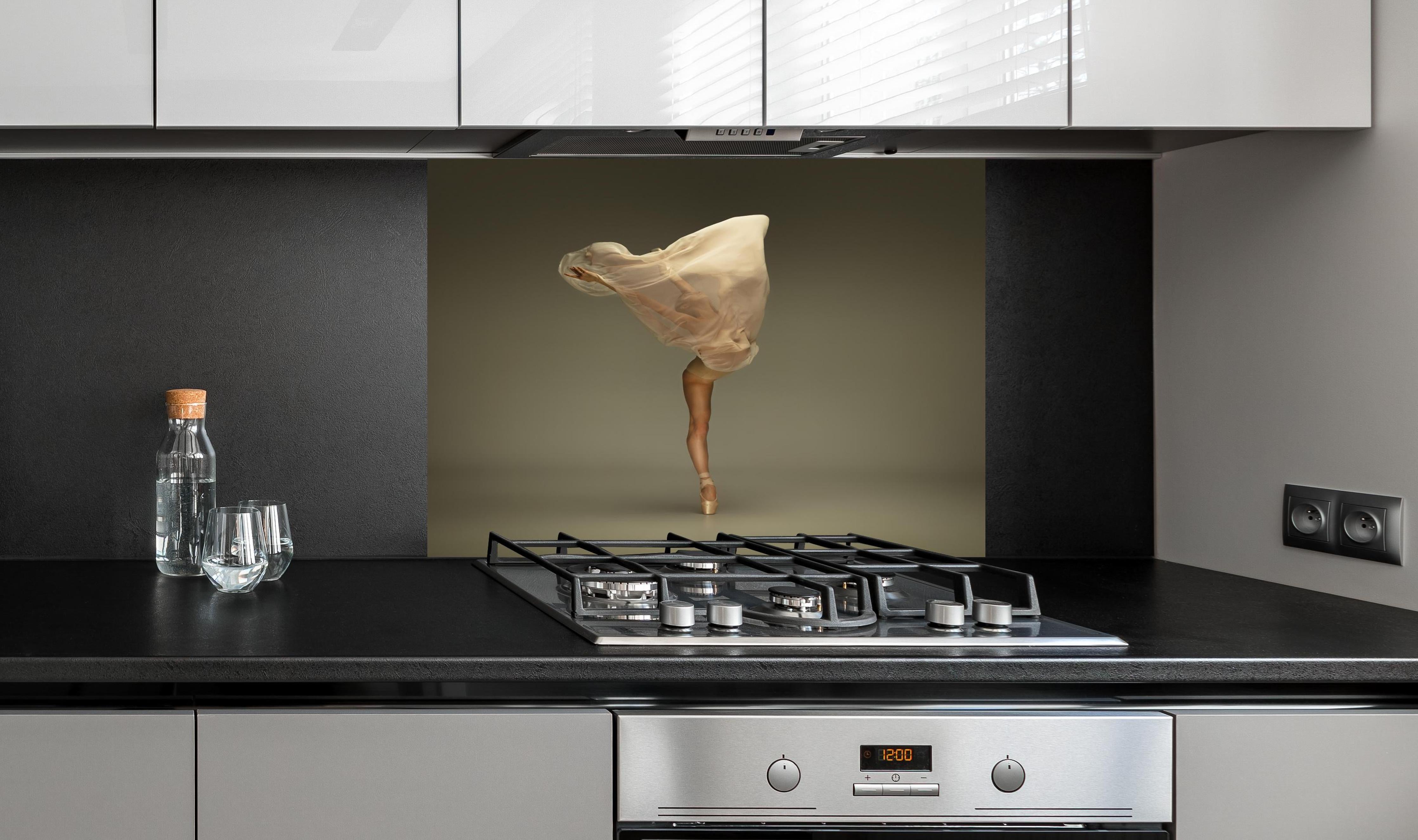 Spritzschutz - Junge Ballerina in grauem Studio hinter einem Cerankochfeld zwischen Holz-Kochutensilien