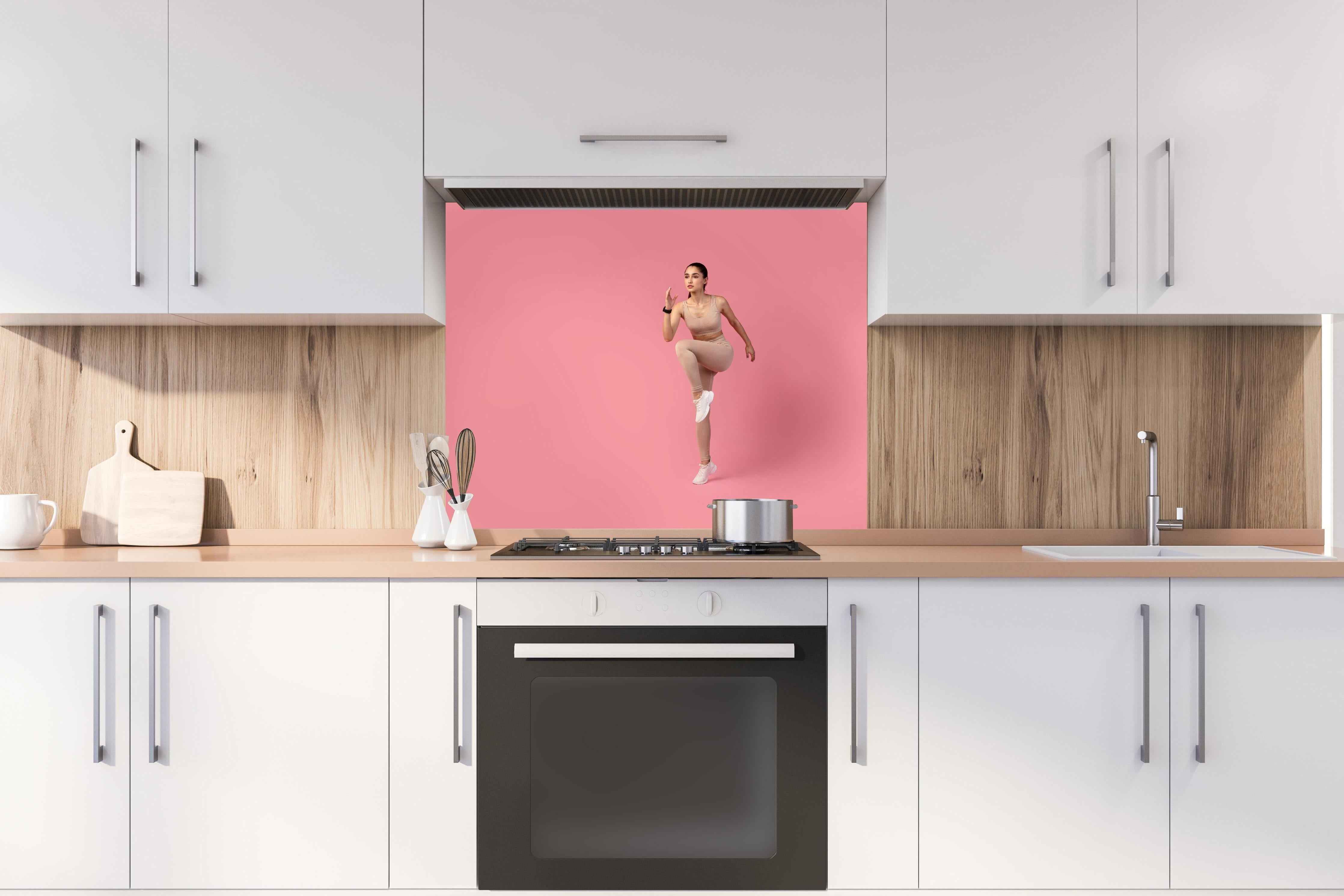 Spritzschutz - Junge Fitness Frau in Läuferpose hinter einem Cerankochfeld zwischen Holz-Kochutensilien