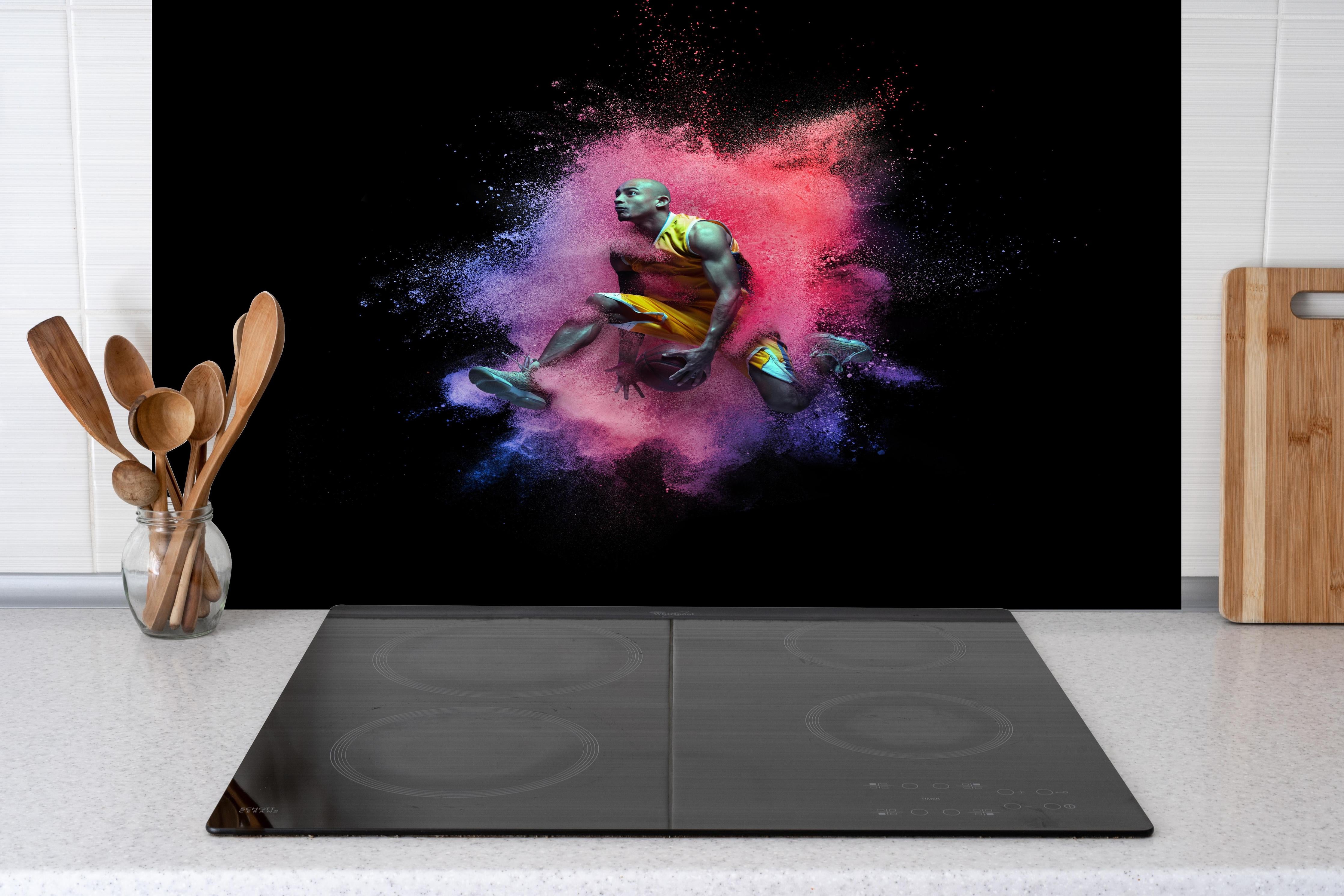 Spritzschutz - Junger Basketballspieler in rötlicher lila Farbexplosion hinter einem Cerankochfeld zwischen Holz-Kochutensilien