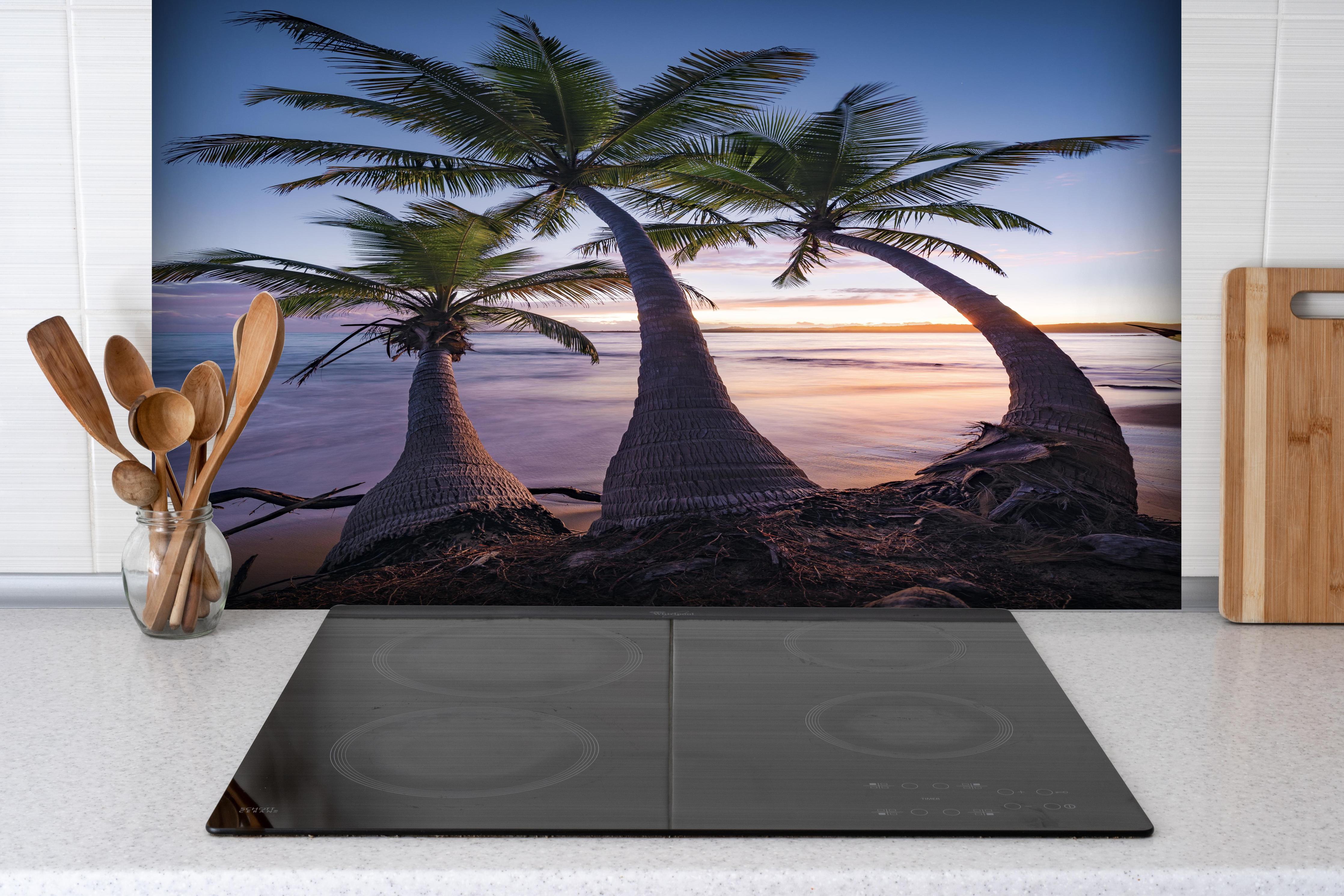 Spritzschutz - Karibik Palmenstrand bei Dämmerung hinter einem Cerankochfeld zwischen Holz-Kochutensilien