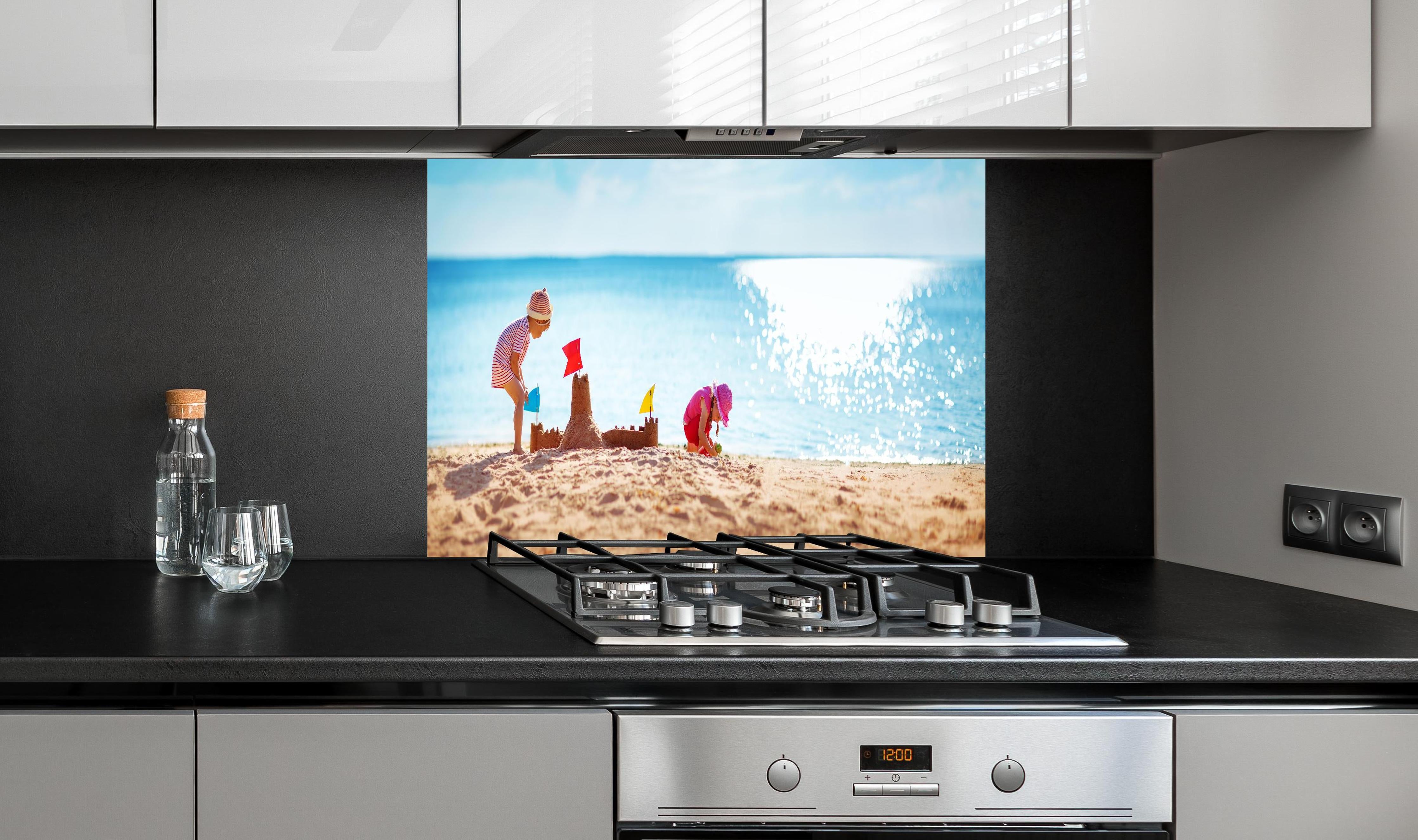 Spritzschutz - Kinder bauen Sandburg am sonnigen Strand hinter einem Cerankochfeld zwischen Holz-Kochutensilien