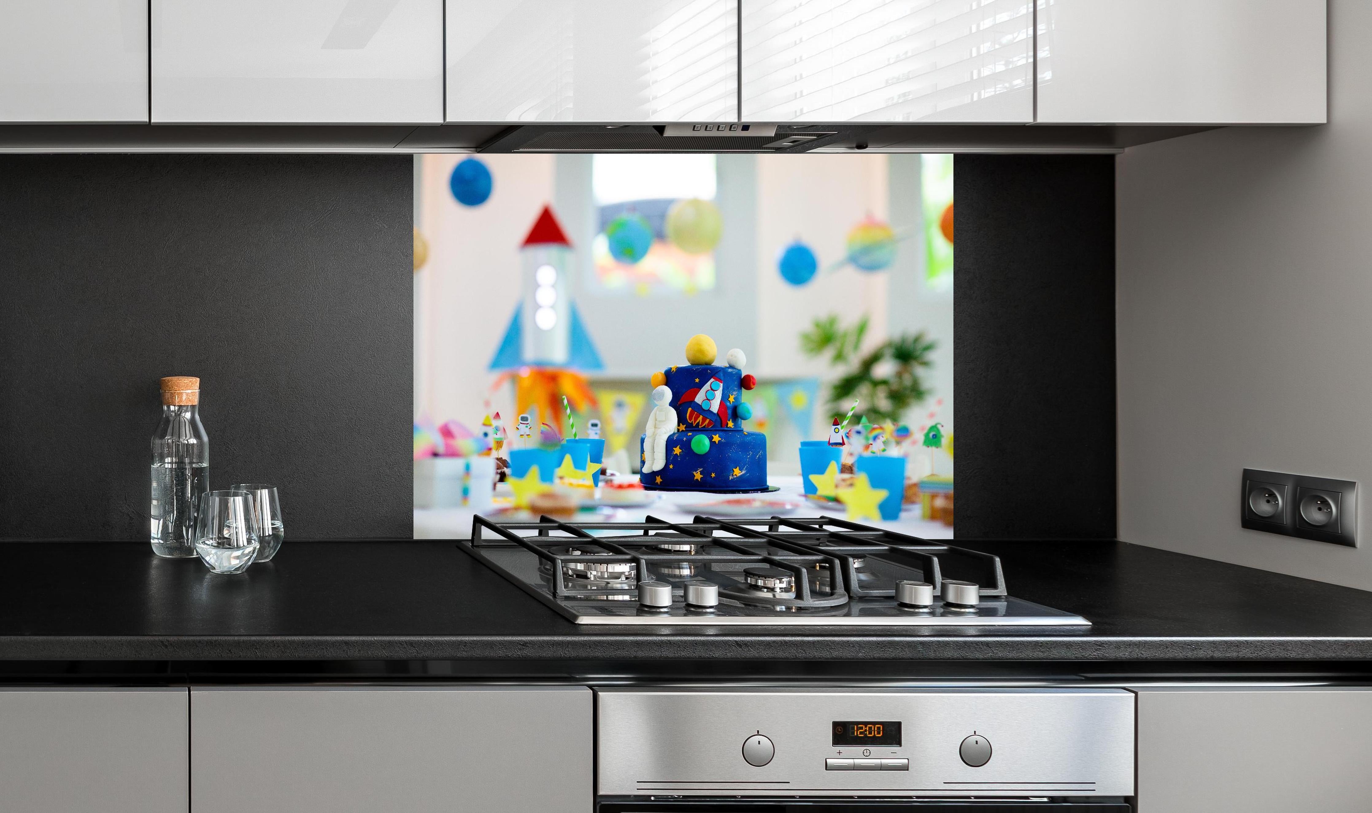 Spritzschutz - Kindergeburtstagsfeier zum Thema Weltraum mit Kuchen. hinter einem Cerankochfeld zwischen Holz-Kochutensilien