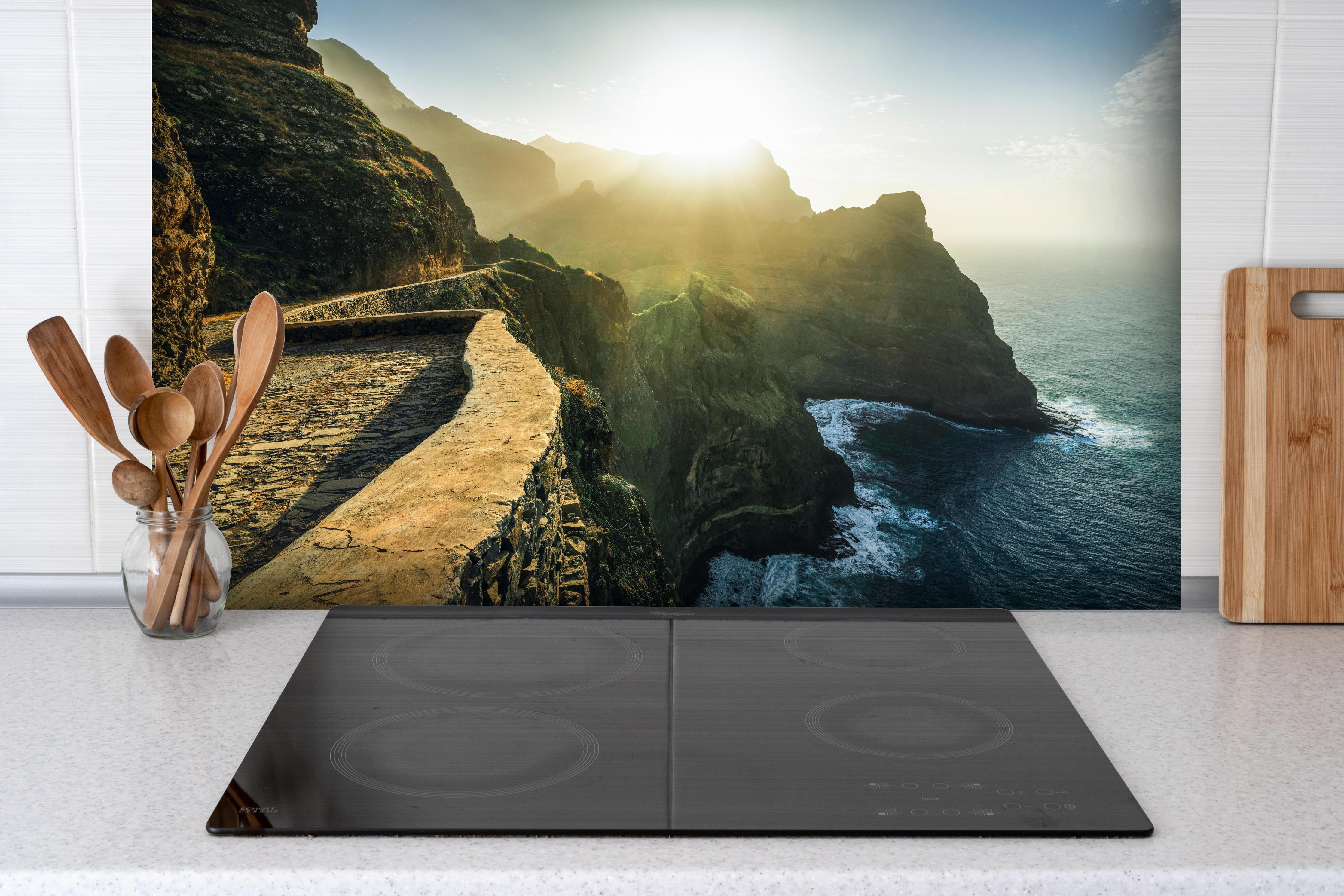 Spritzschutz - Kliff-Pfad im Sonnenlicht am Meer hinter einem Cerankochfeld zwischen Holz-Kochutensilien