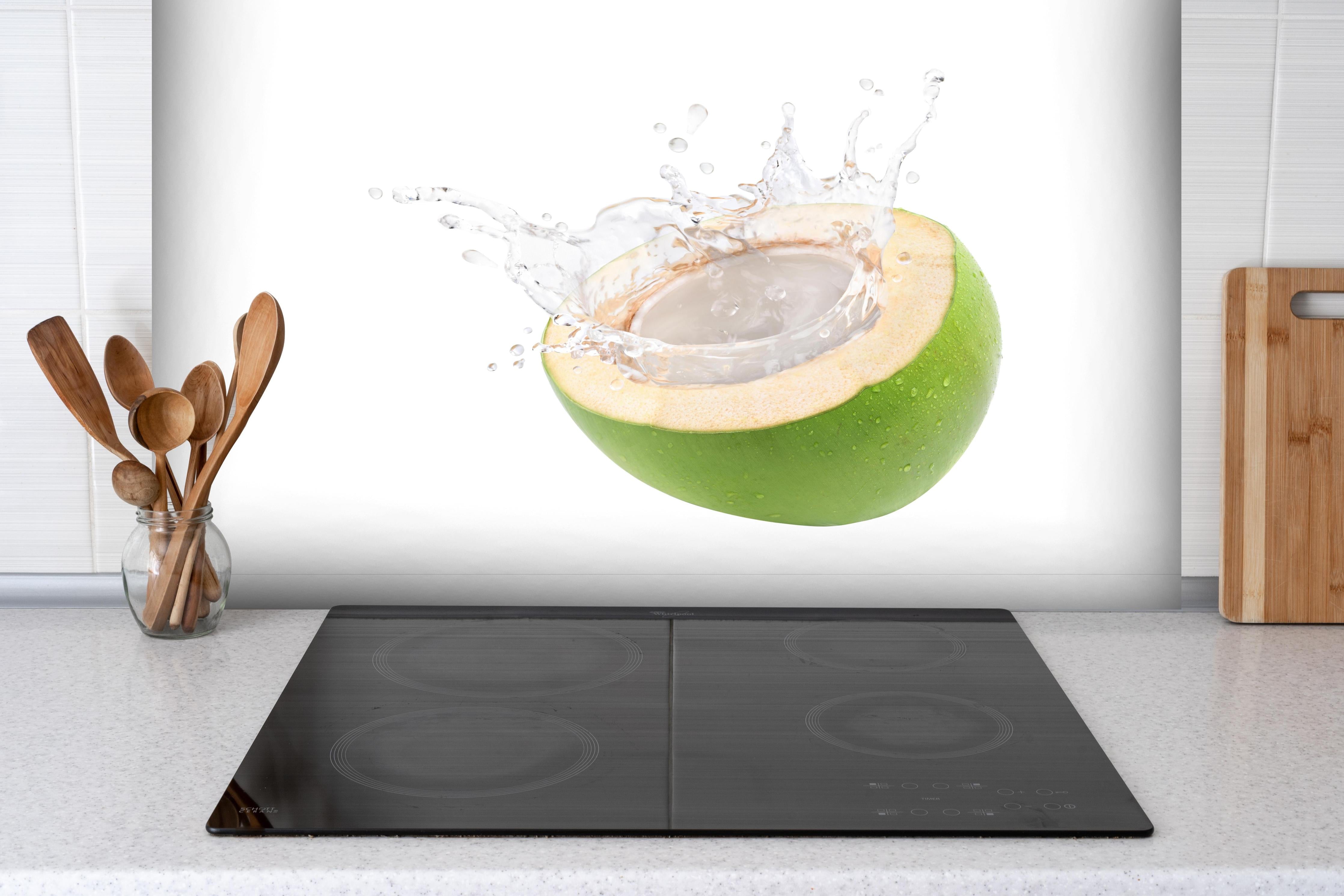Spritzschutz - Kokosnuss mit Kokosmilch hinter einem Cerankochfeld zwischen Holz-Kochutensilien