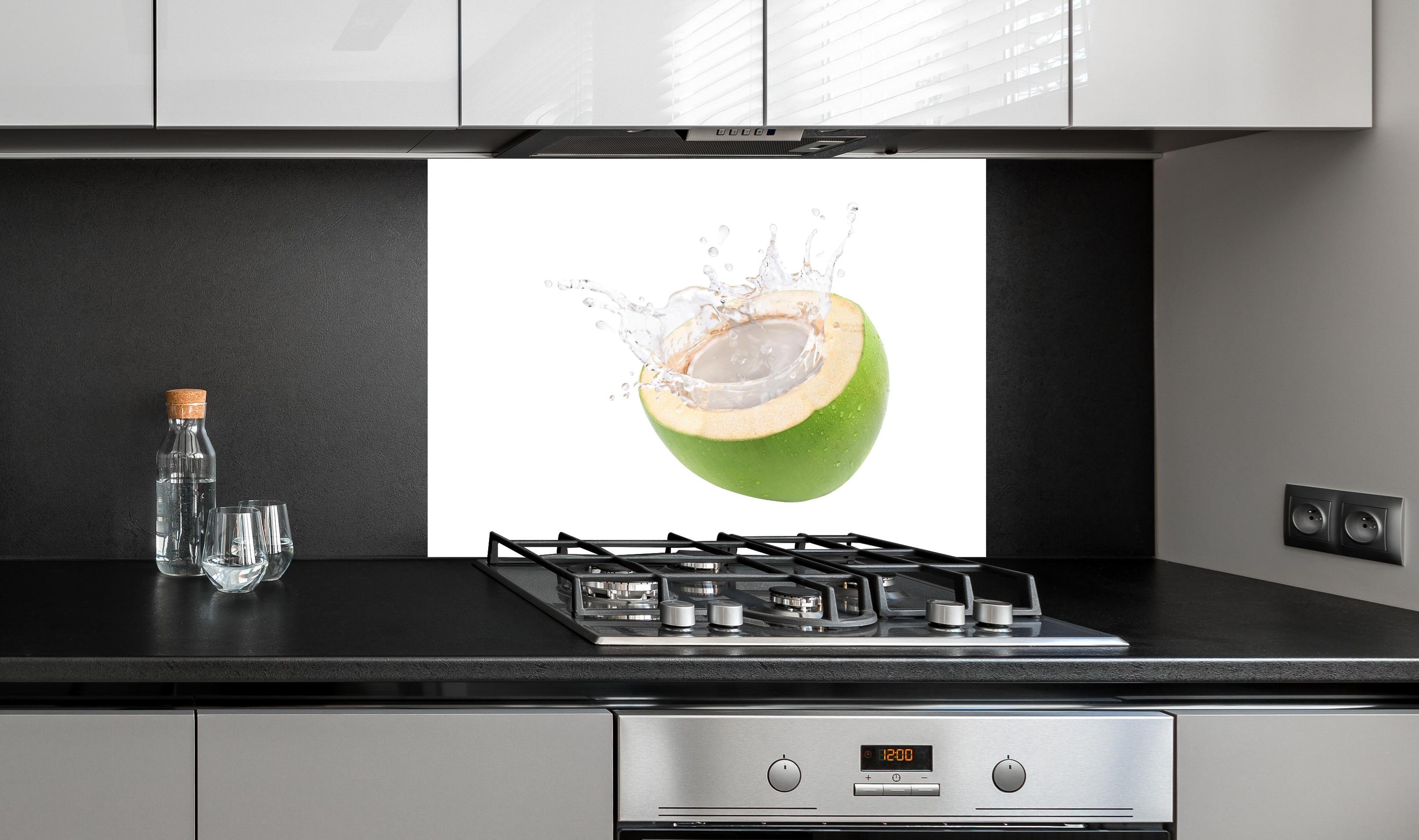 Spritzschutz - Kokosnuss mit Kokosmilch hinter einem Cerankochfeld zwischen Holz-Kochutensilien