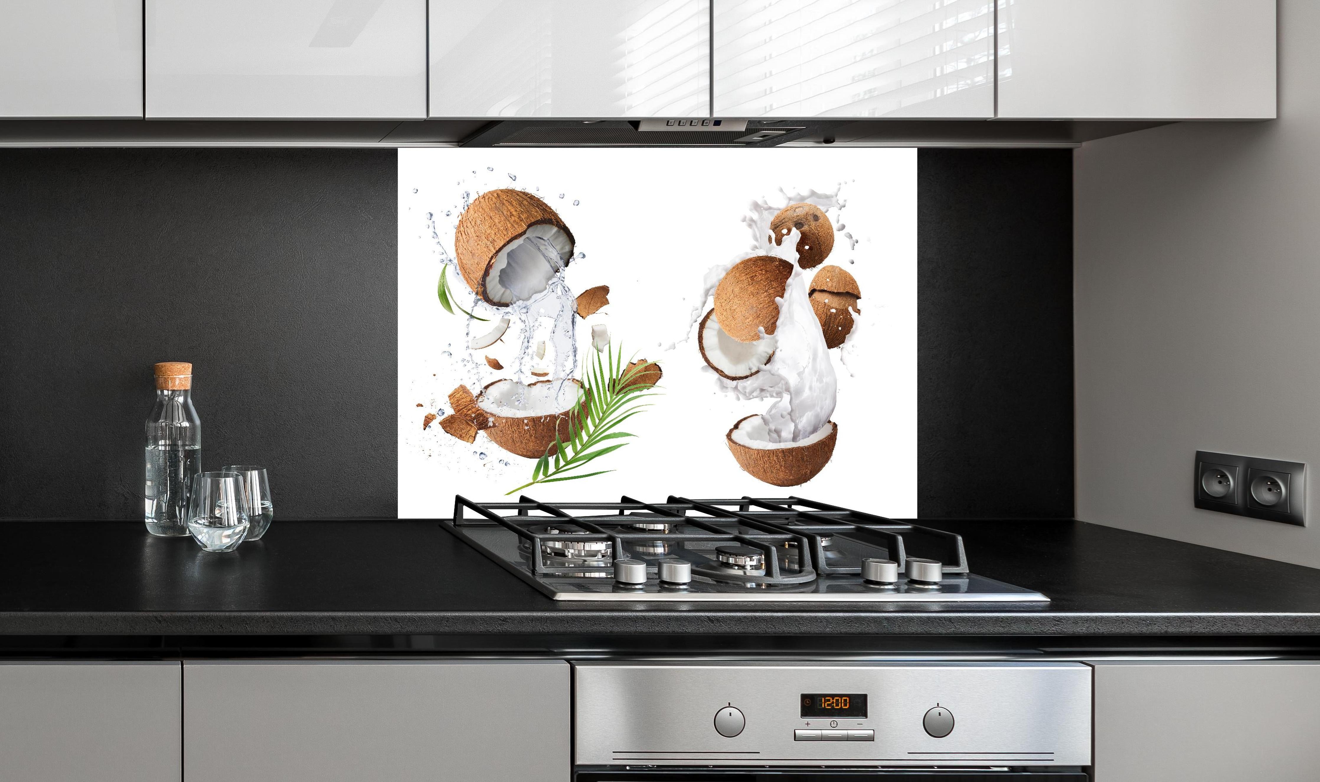 Spritzschutz - Kokosnuss mit frischem Milchspritzer hinter einem Cerankochfeld zwischen Holz-Kochutensilien