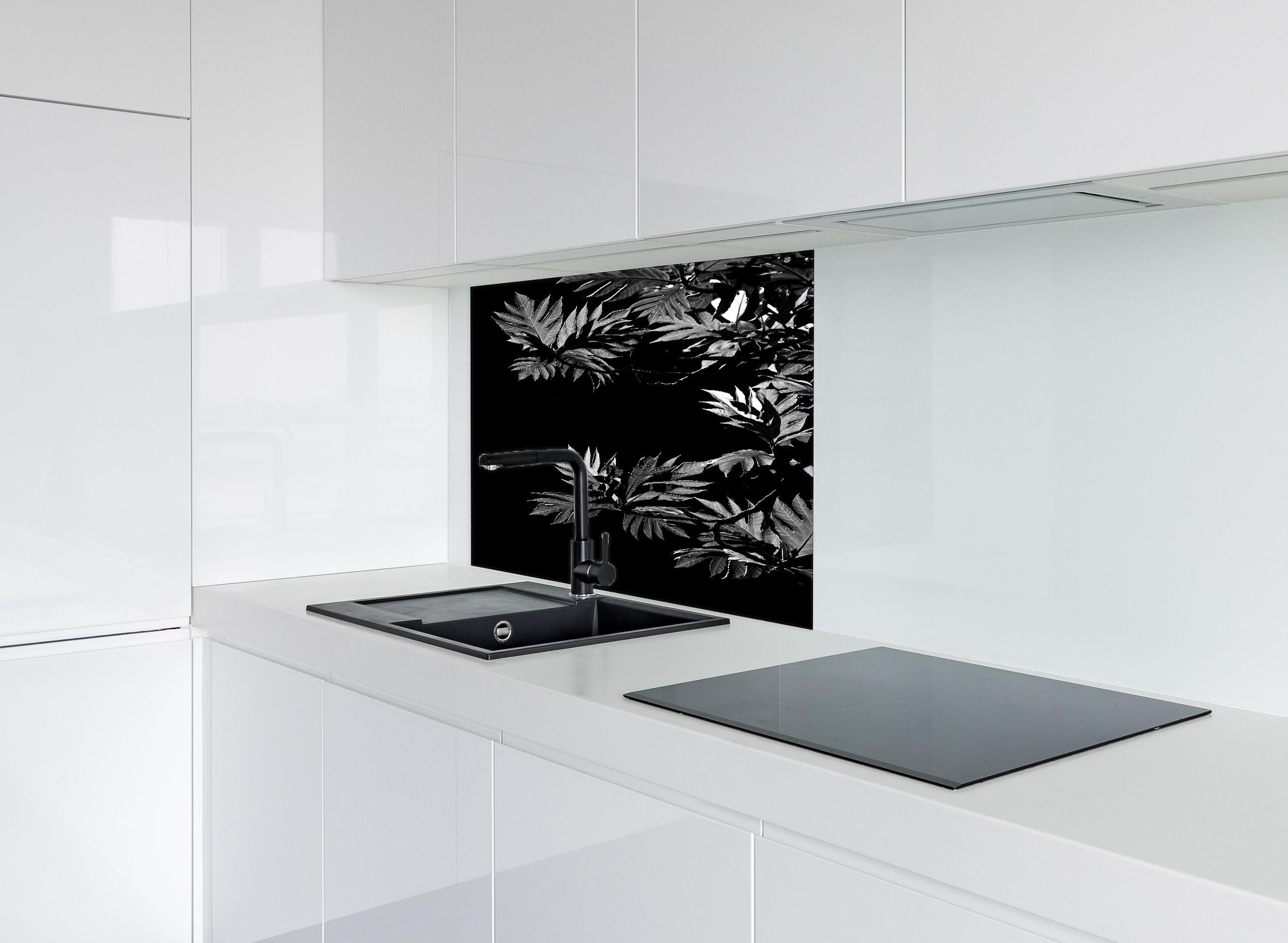 Spritzschutz - Kontrastreiche Blätter auf schwarzem Hintergrund hinter einem Cerankochfeld zwischen Holz-Kochutensilien