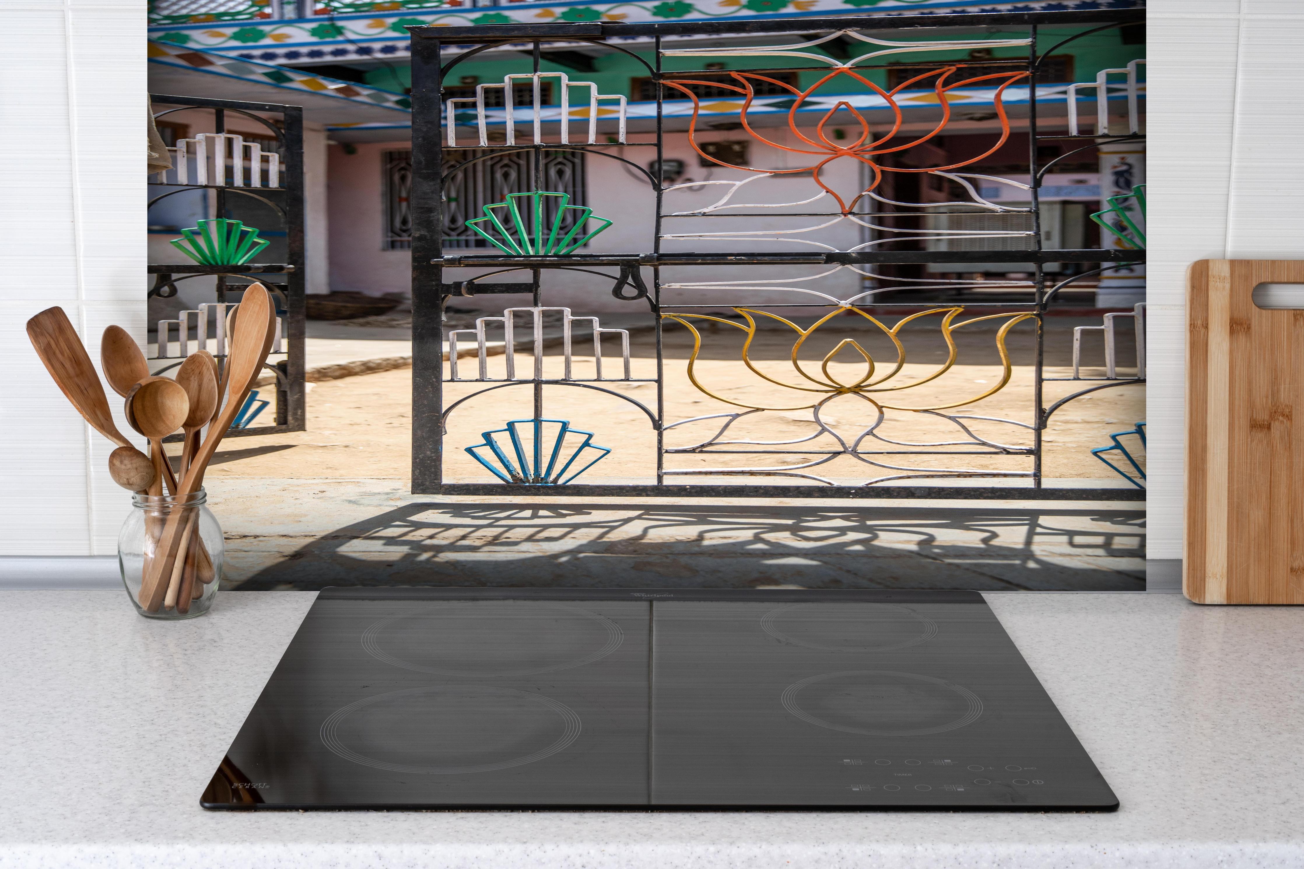 Spritzschutz - Künstlerisches Lotus-Tor gegen Hausfassade hinter einem Cerankochfeld zwischen Holz-Kochutensilien