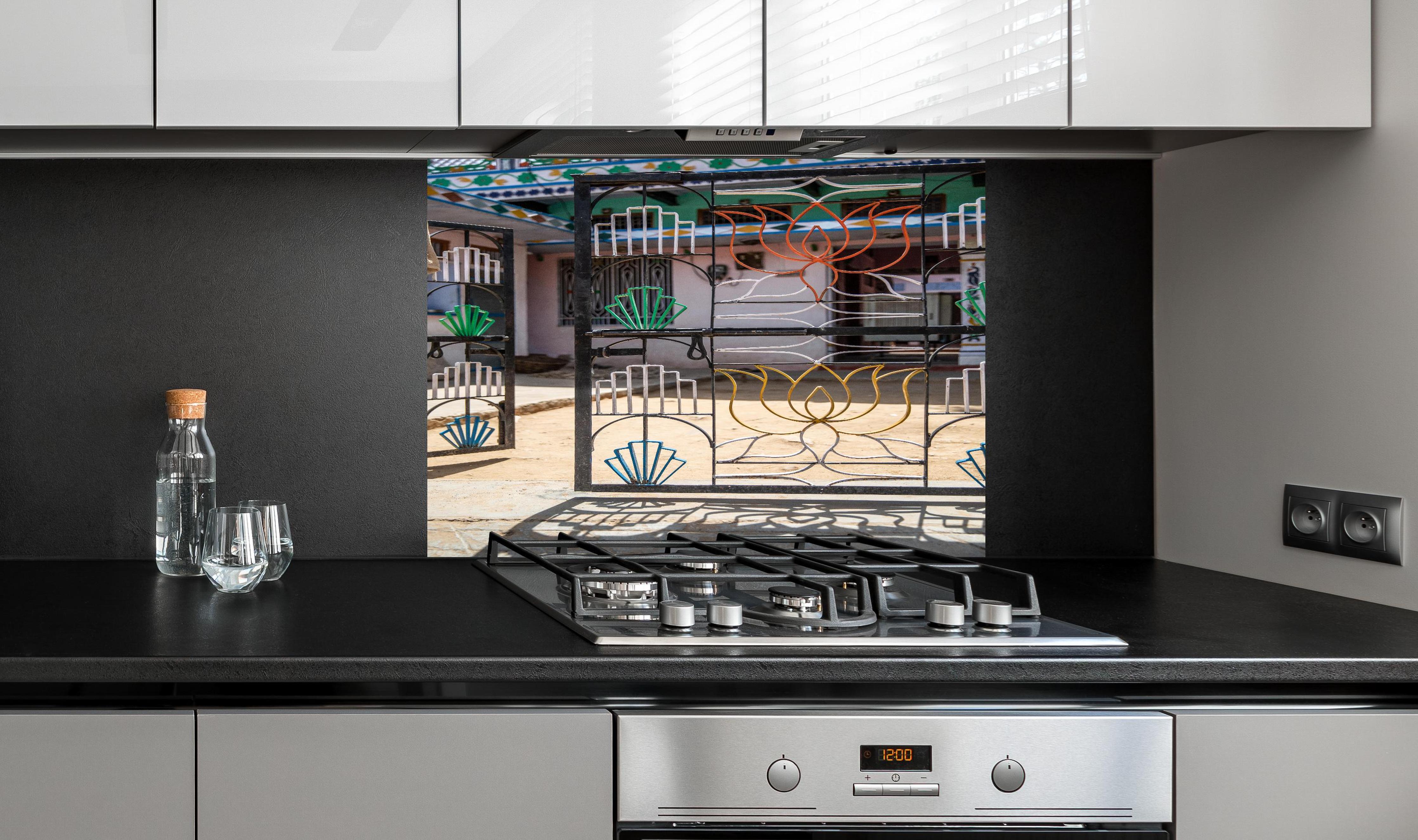 Spritzschutz - Künstlerisches Lotus-Tor gegen Hausfassade hinter einem Cerankochfeld zwischen Holz-Kochutensilien