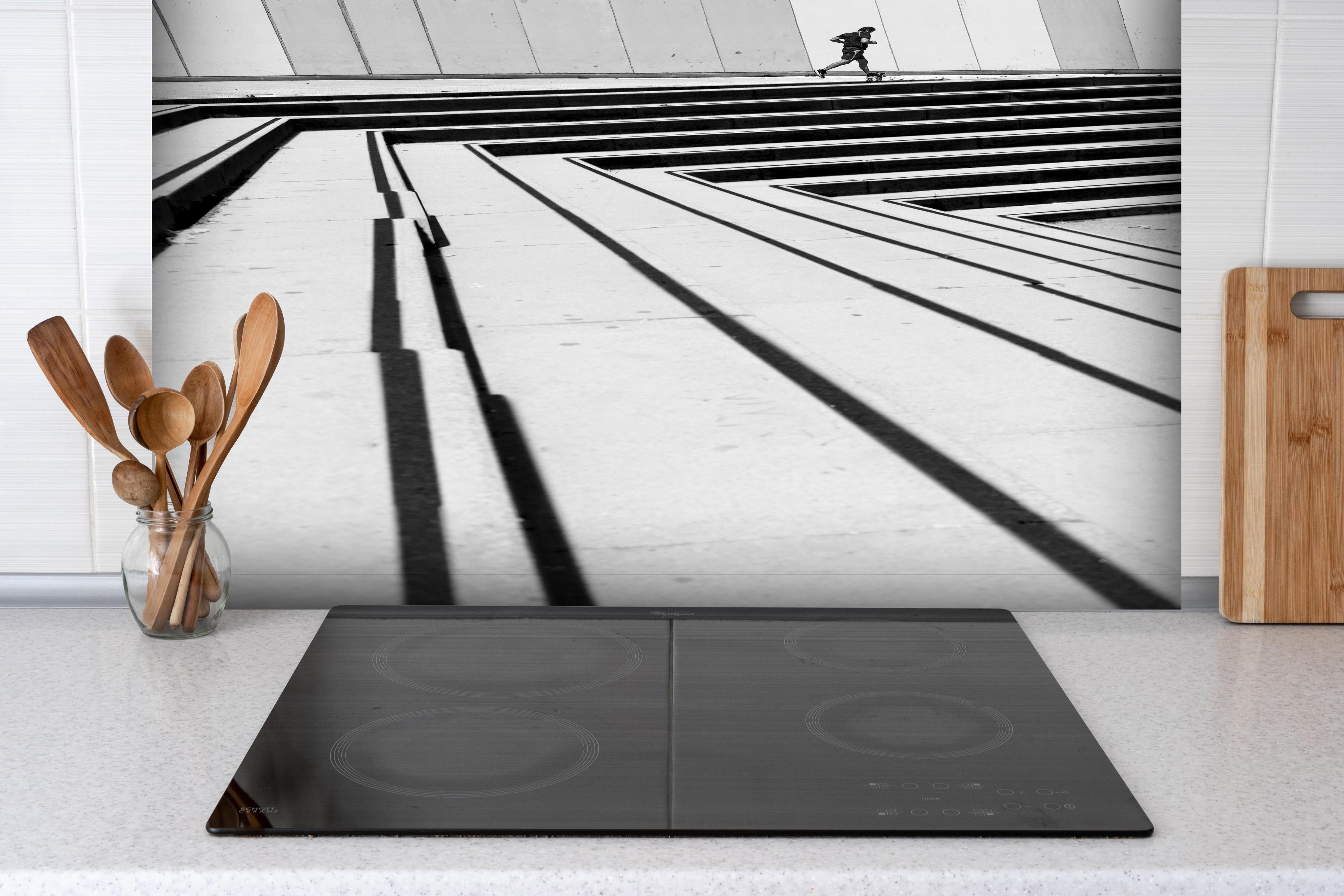 Spritzschutz - Läufer im Spiel der Schatten und Linien hinter einem Cerankochfeld zwischen Holz-Kochutensilien