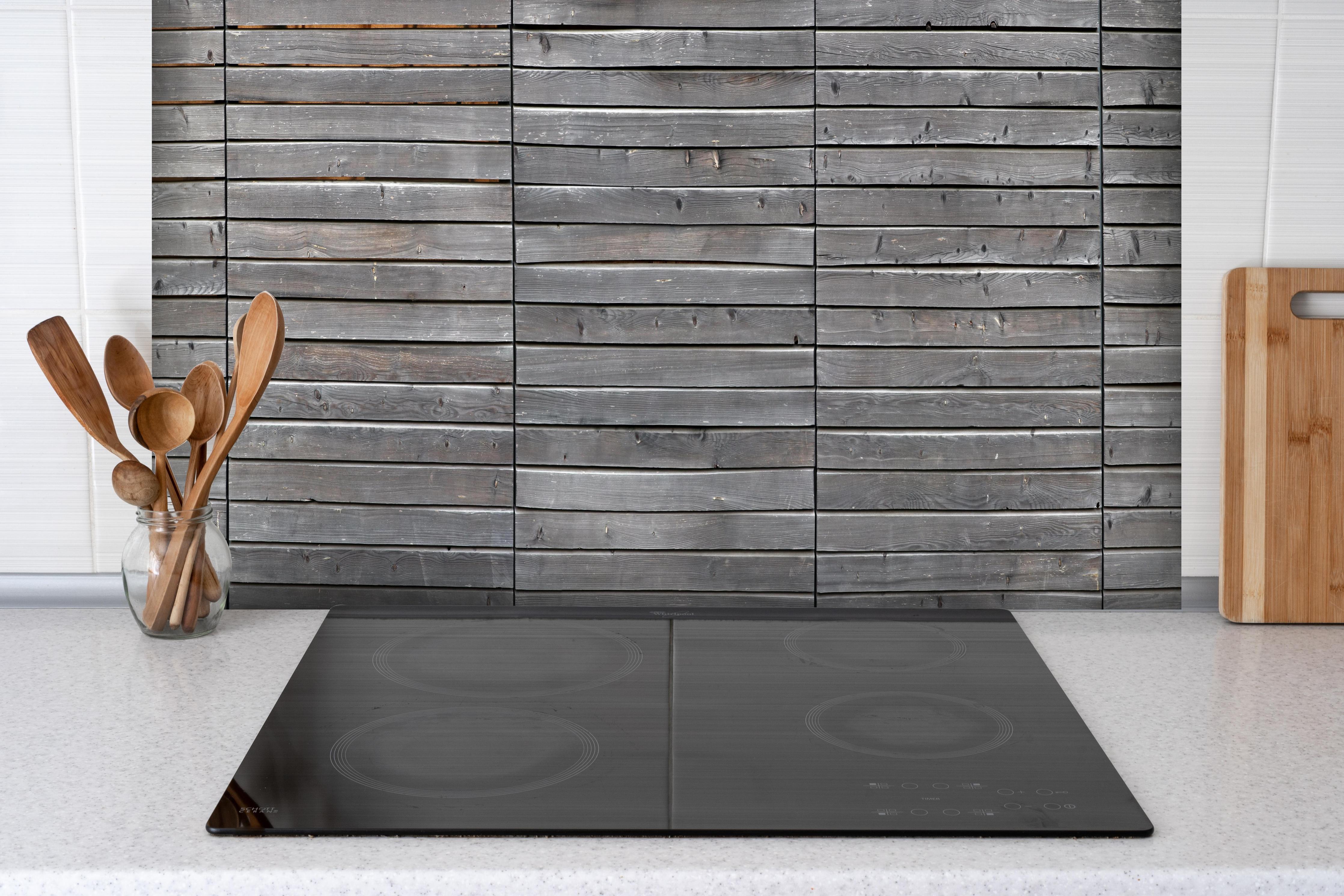 Spritzschutz - Langer grauer Holzzaun hinter einem Cerankochfeld zwischen Holz-Kochutensilien