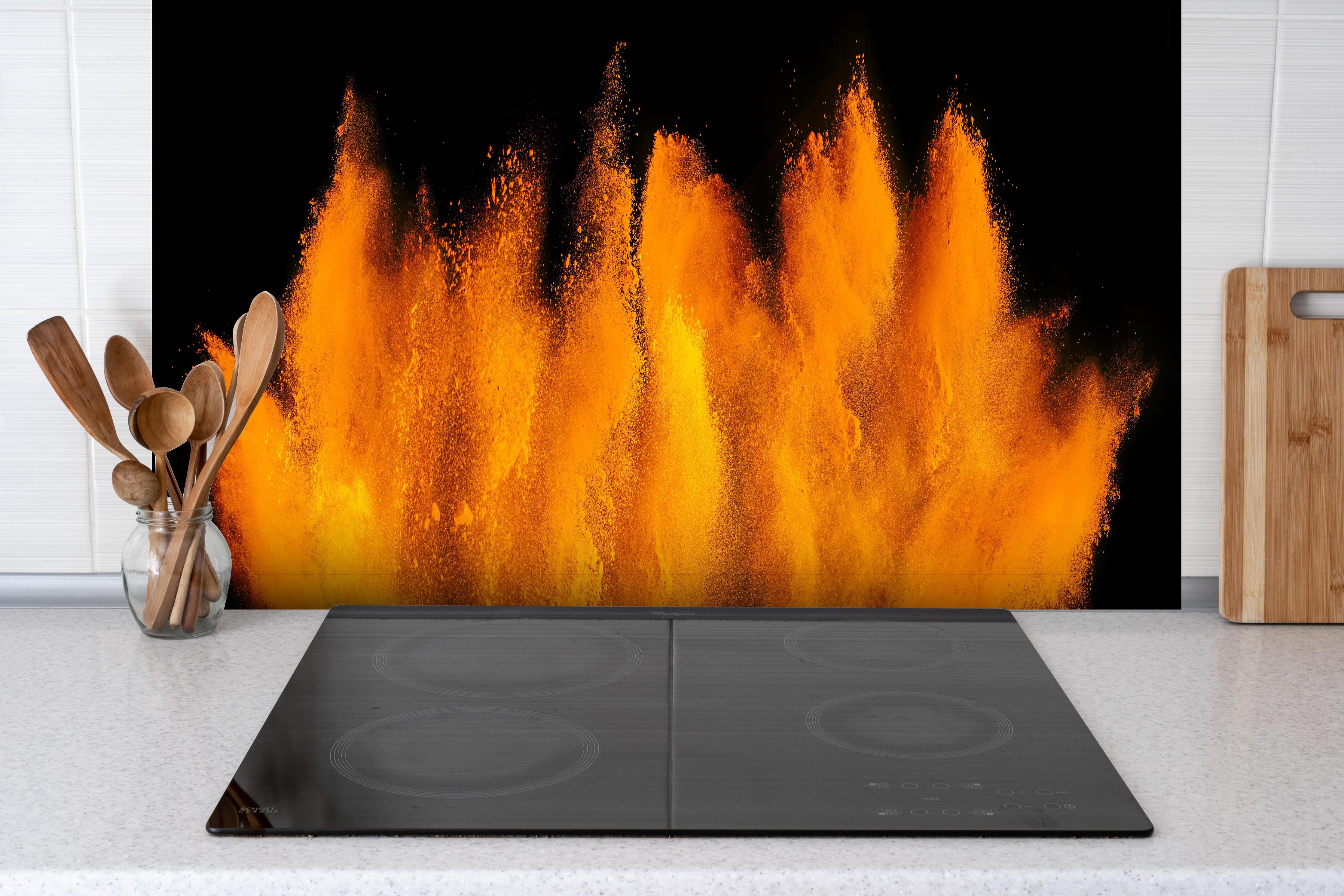 Spritzschutz - Lebendige Holi Farbexplosion auf Schwarz hinter einem Cerankochfeld zwischen Holz-Kochutensilien