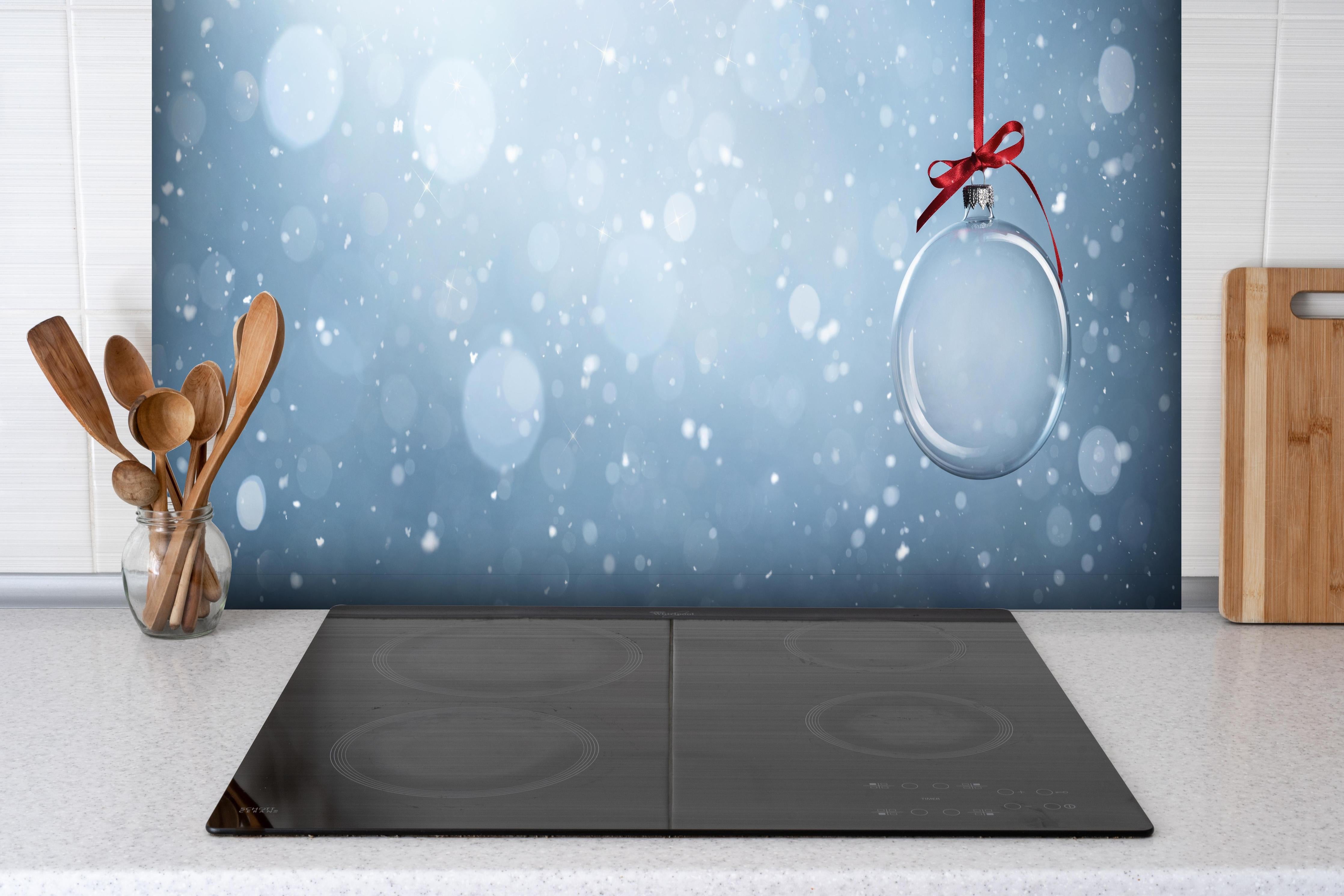 Spritzschutz - Leere Weihnachtskugel hinter einem Cerankochfeld zwischen Holz-Kochutensilien