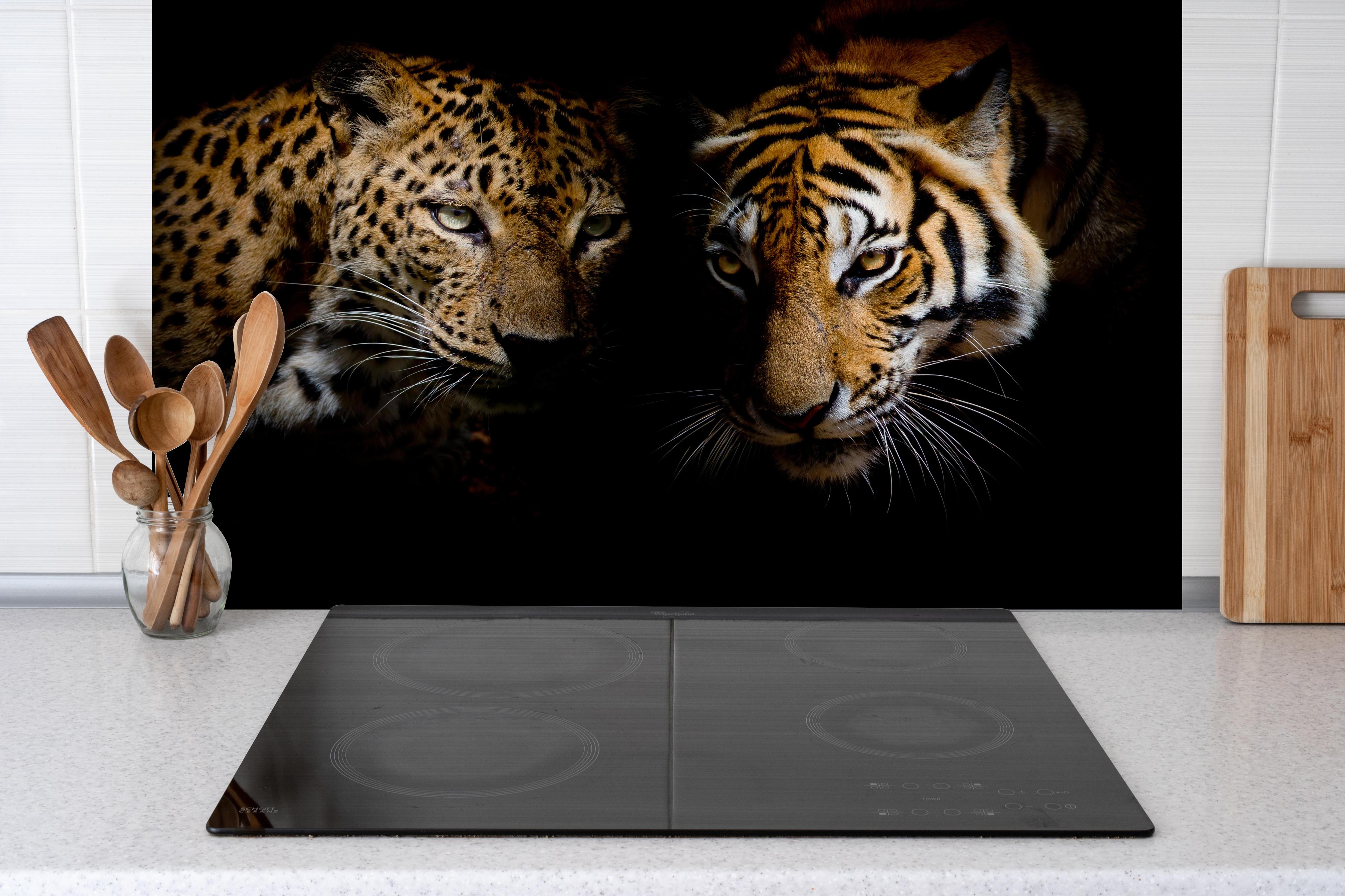 Spritzschutz - Leopard und Tiger isoliert auf schwarzen Hintergrund hinter einem Cerankochfeld zwischen Holz-Kochutensilien