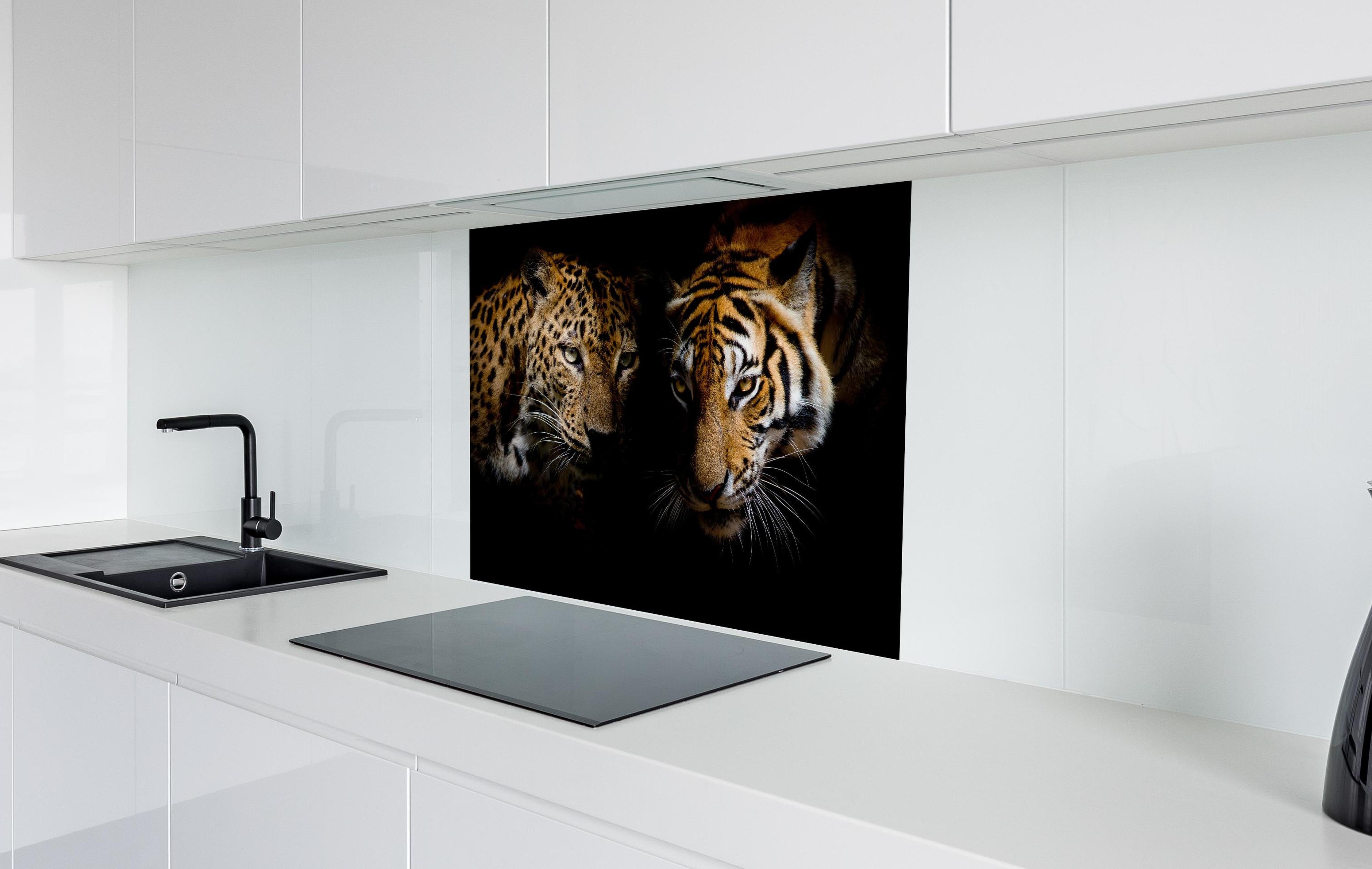 Spritzschutz - Leopard und Tiger isoliert auf schwarzen Hintergrund hinter einem Cerankochfeld zwischen Holz-Kochutensilien