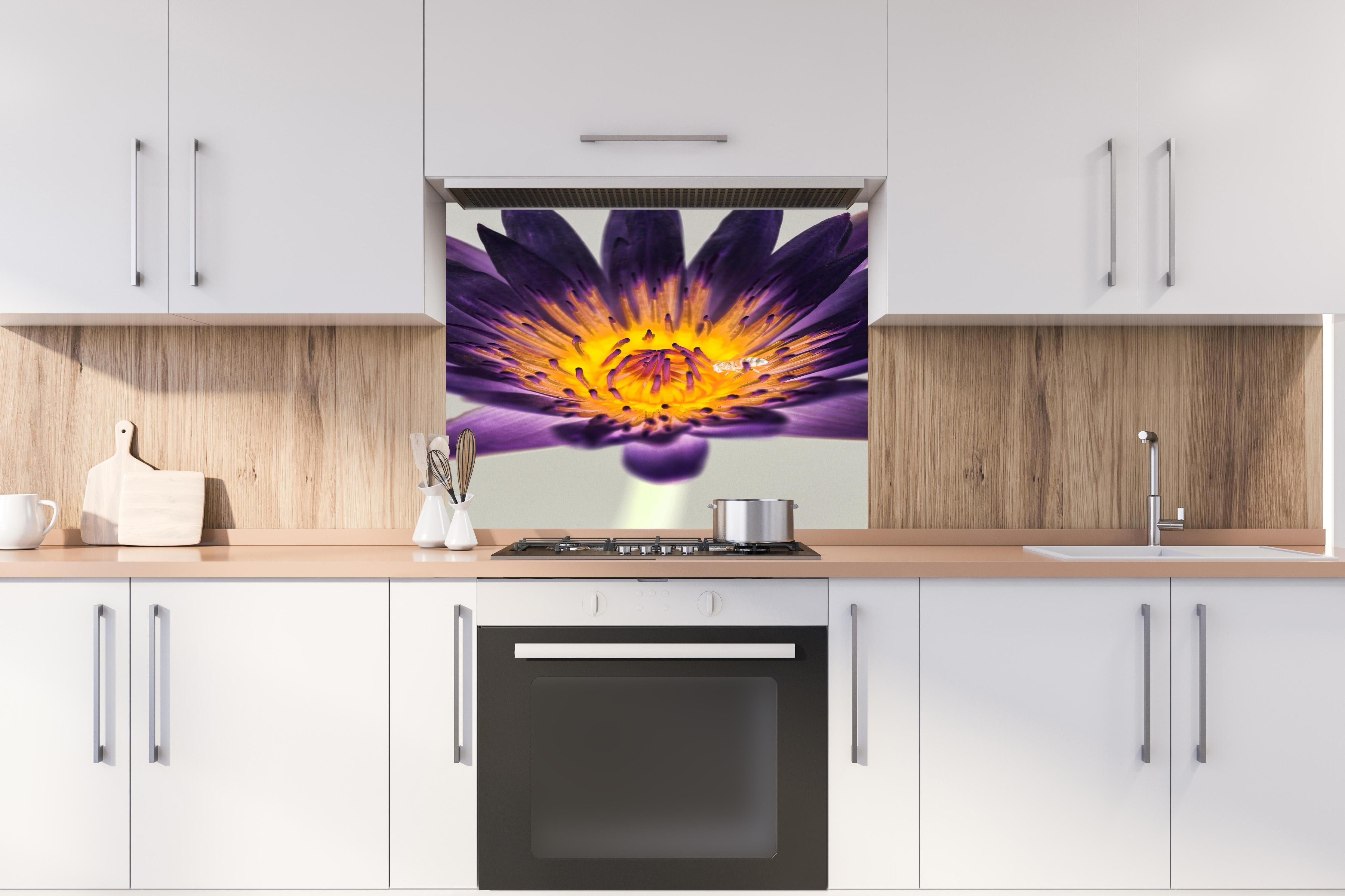 Spritzschutz - Leuchtende Lila Wasserlilie mit gelbem Kern Makro hinter einem Cerankochfeld zwischen Holz-Kochutensilien