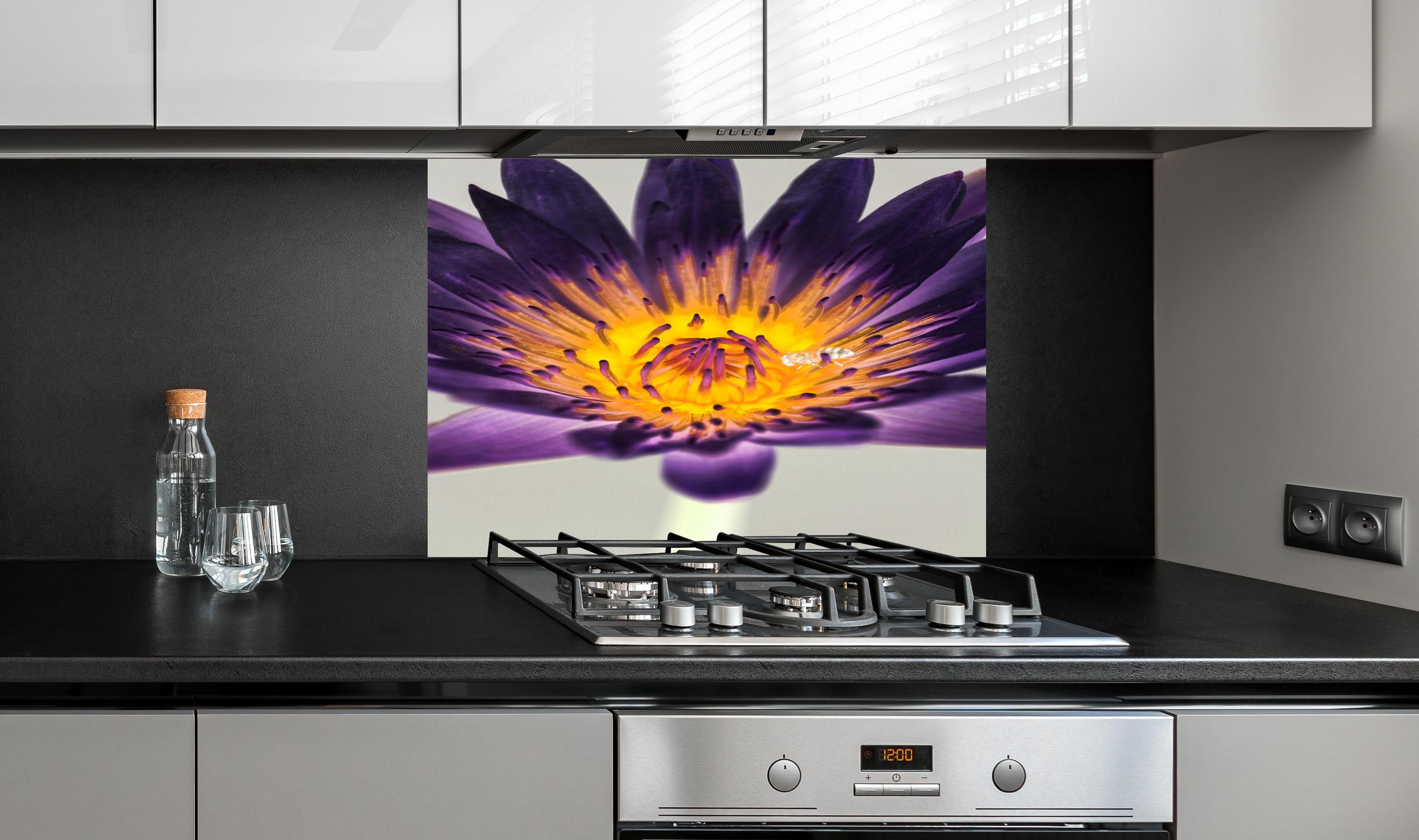 Spritzschutz - Leuchtende Lila Wasserlilie mit gelbem Kern Makro hinter einem Cerankochfeld zwischen Holz-Kochutensilien