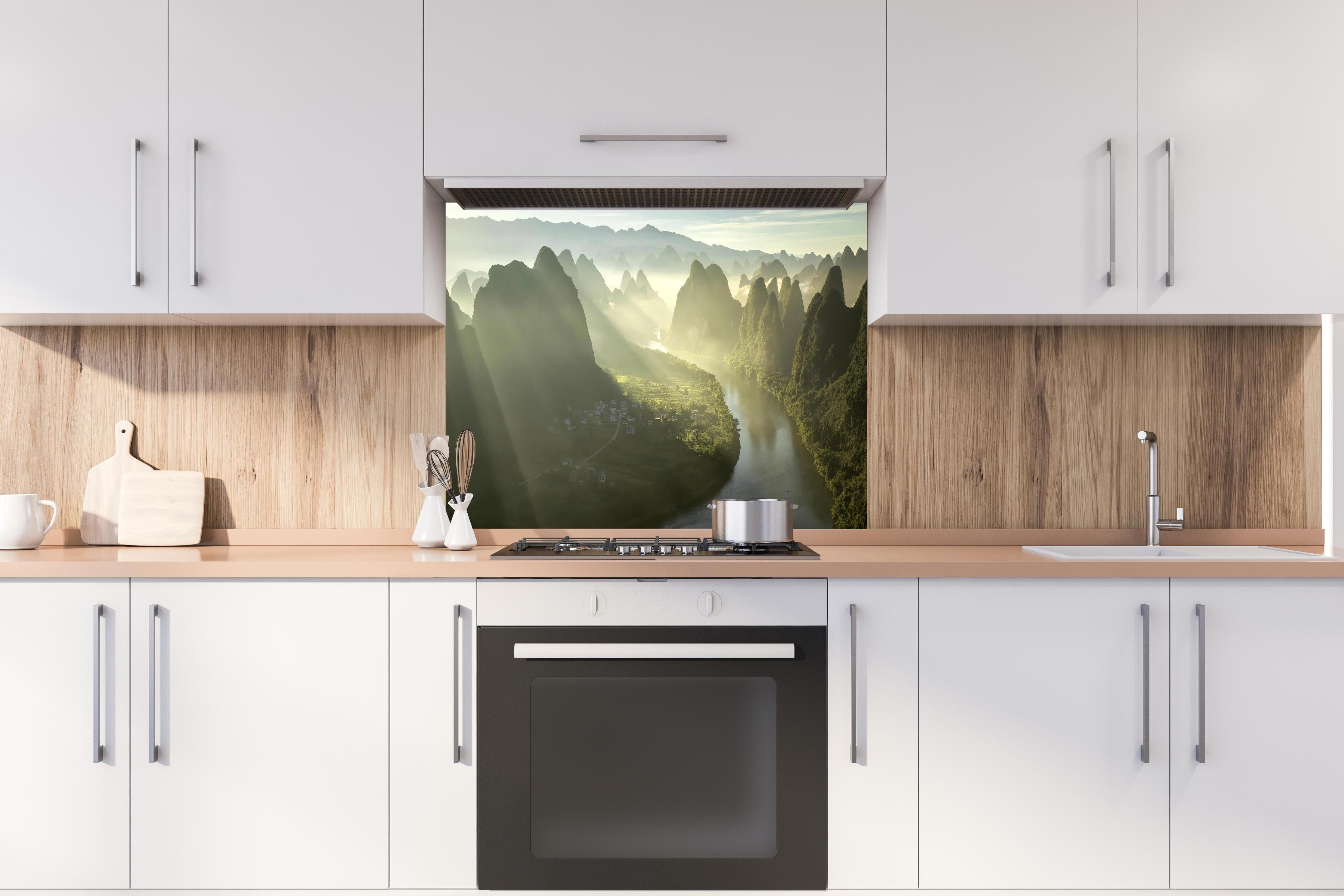 Spritzschutz - Lichtstrahlen über Li-Fluss und Karstberge hinter einem Cerankochfeld zwischen Holz-Kochutensilien