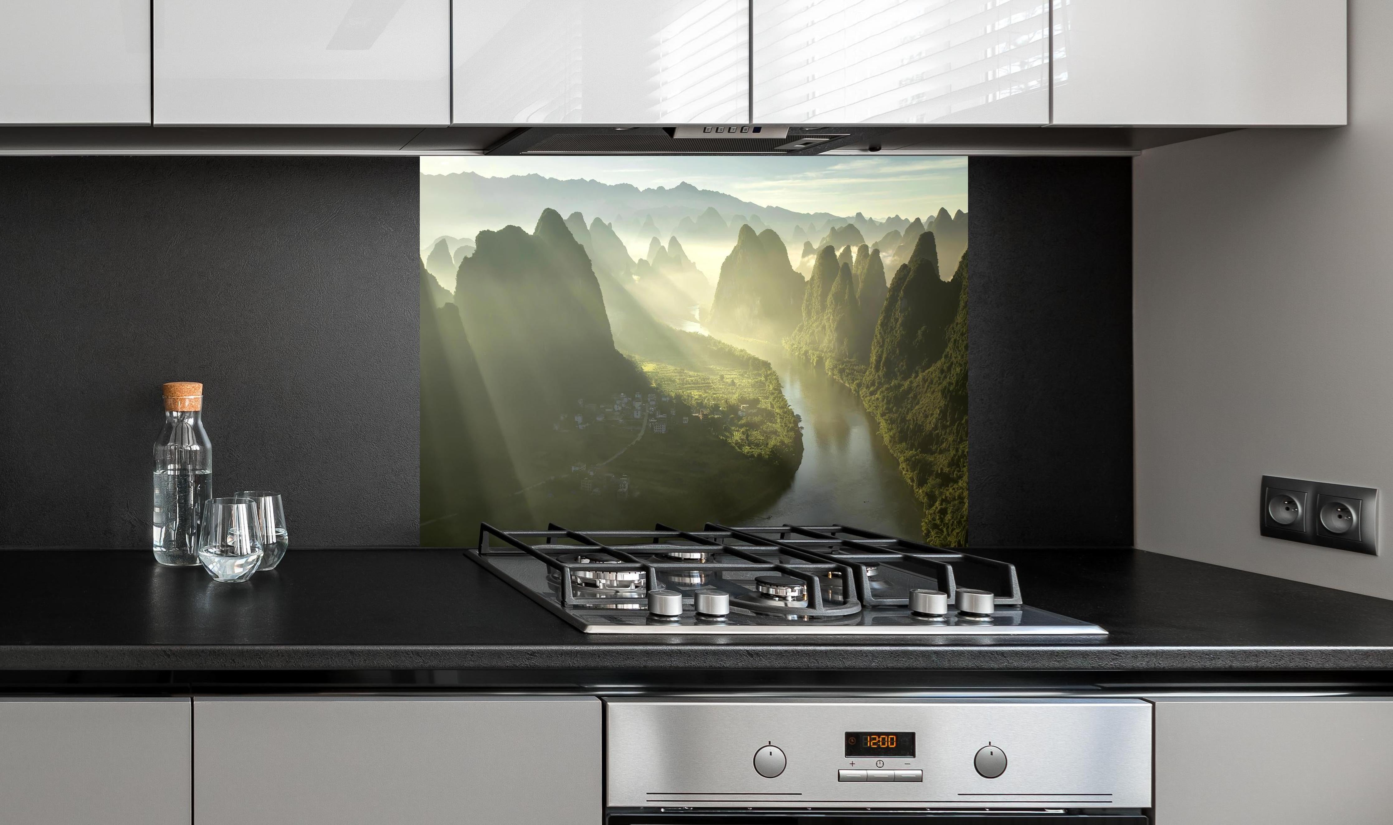 Spritzschutz - Lichtstrahlen über Li-Fluss und Karstberge hinter einem Cerankochfeld zwischen Holz-Kochutensilien