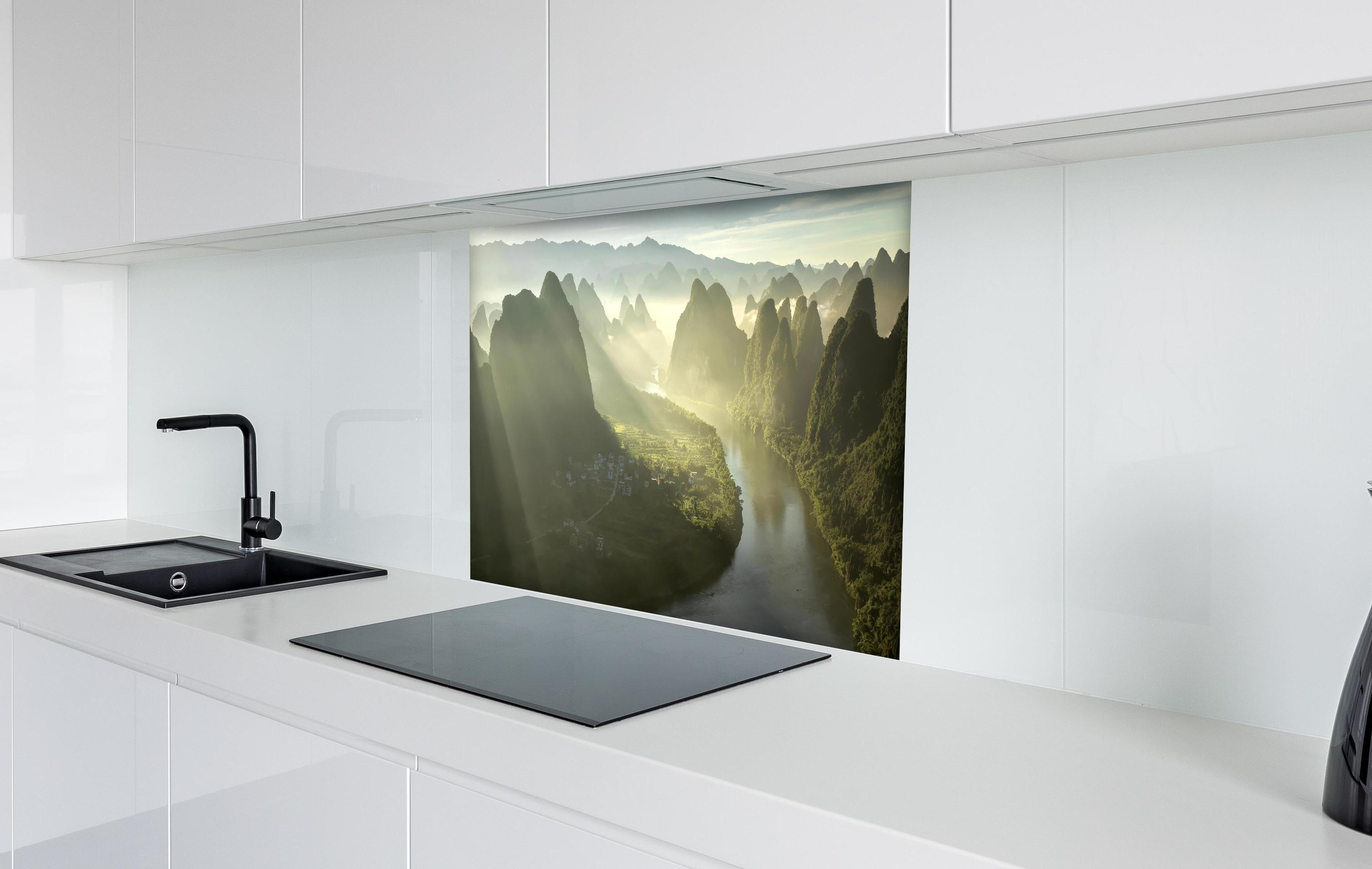 Spritzschutz - Lichtstrahlen über Li-Fluss und Karstberge hinter einem Cerankochfeld zwischen Holz-Kochutensilien