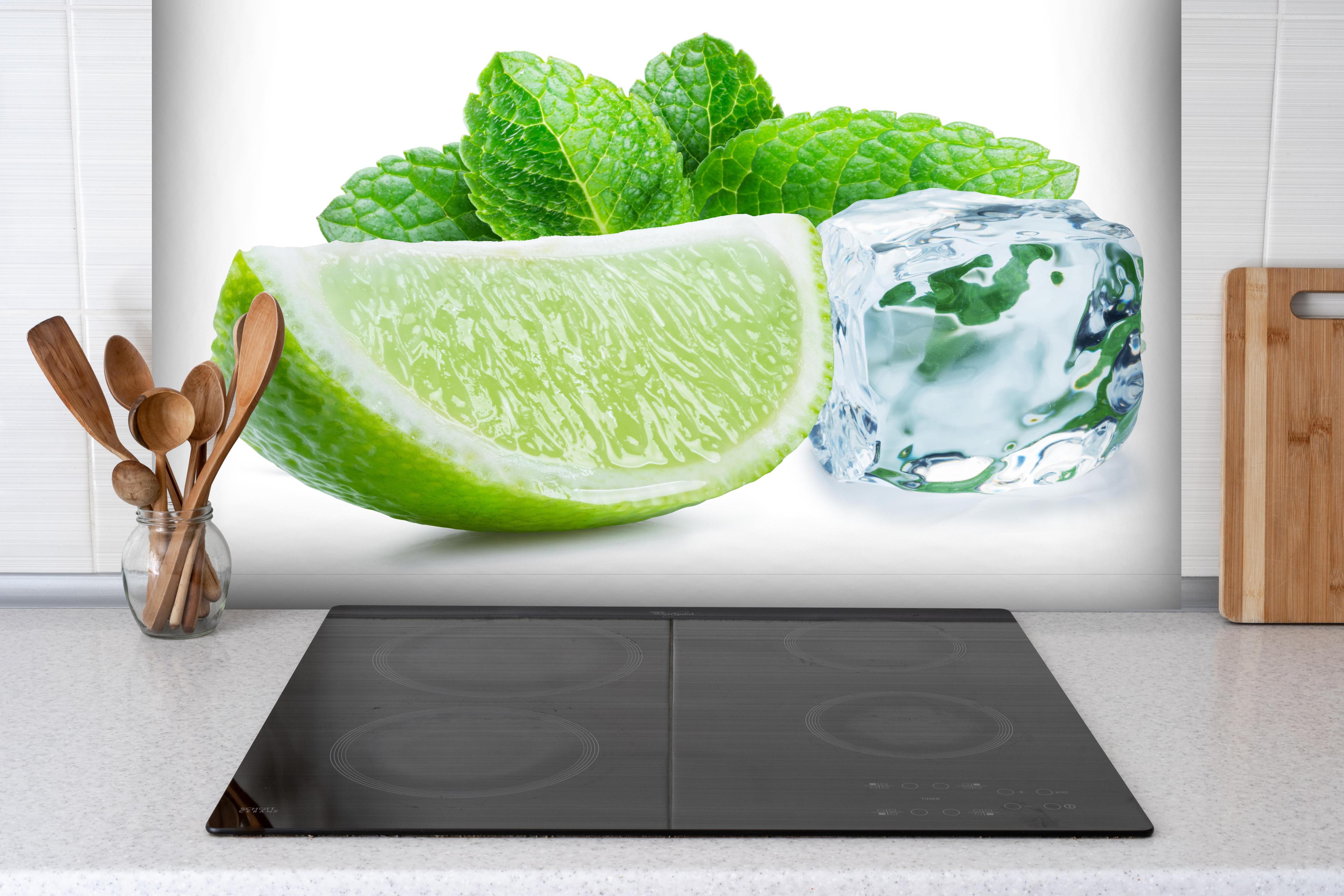 Spritzschutz - Limettenscheibe mit Eis und Minze hinter einem Cerankochfeld zwischen Holz-Kochutensilien