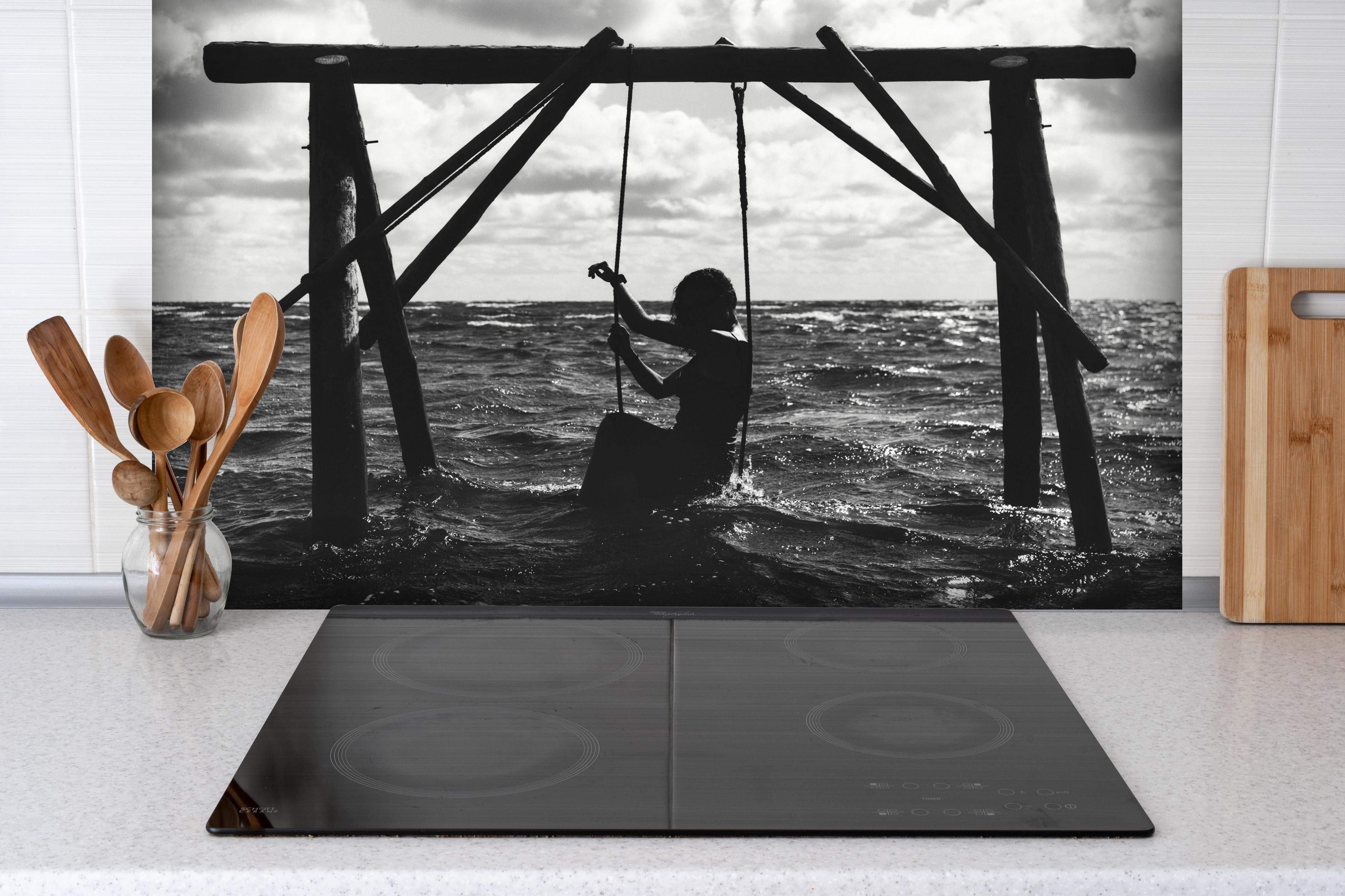 Spritzschutz - Mädchen auf Schaukel im Wasser hinter einem Cerankochfeld zwischen Holz-Kochutensilien