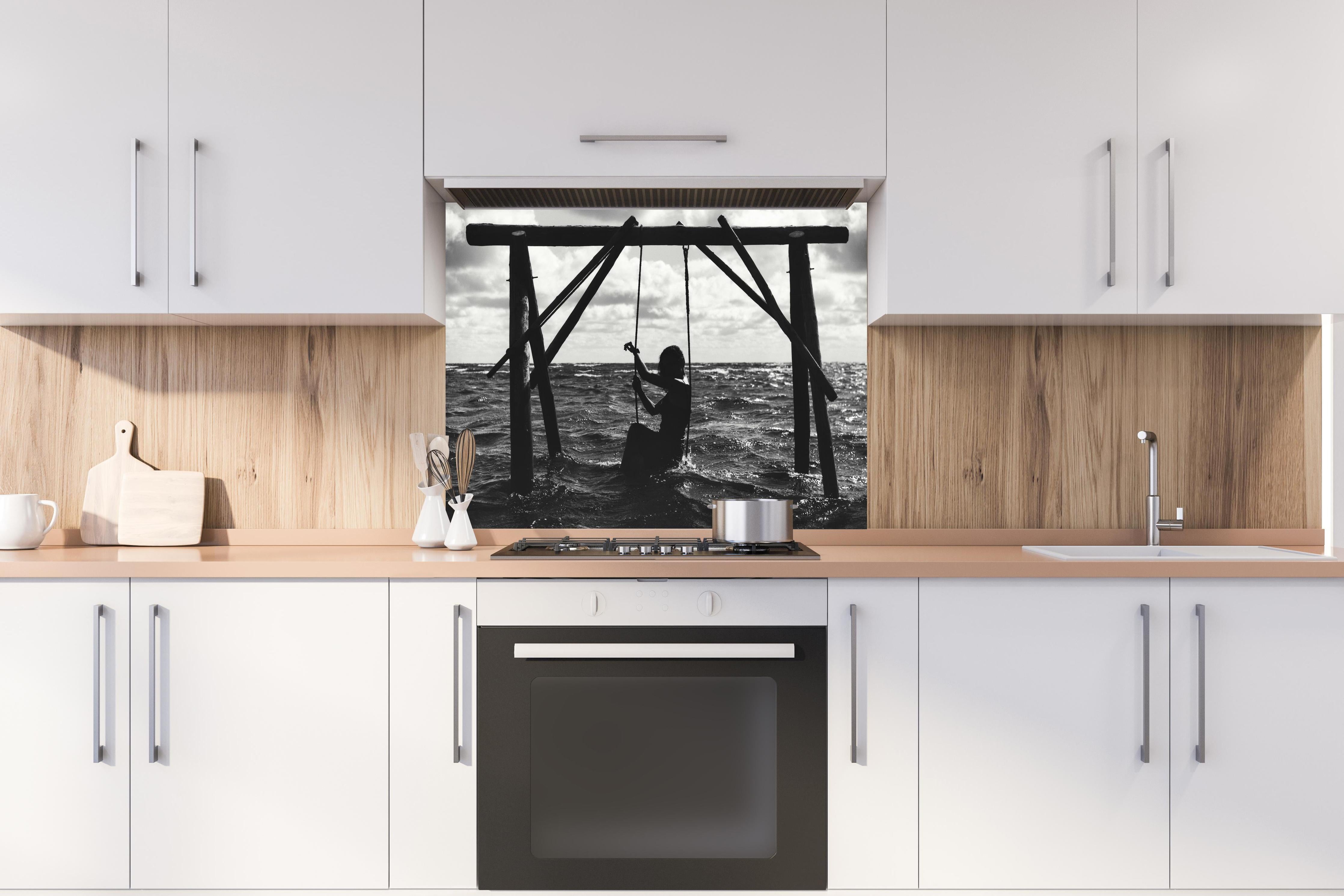 Spritzschutz - Mädchen auf Schaukel im Wasser hinter einem Cerankochfeld zwischen Holz-Kochutensilien