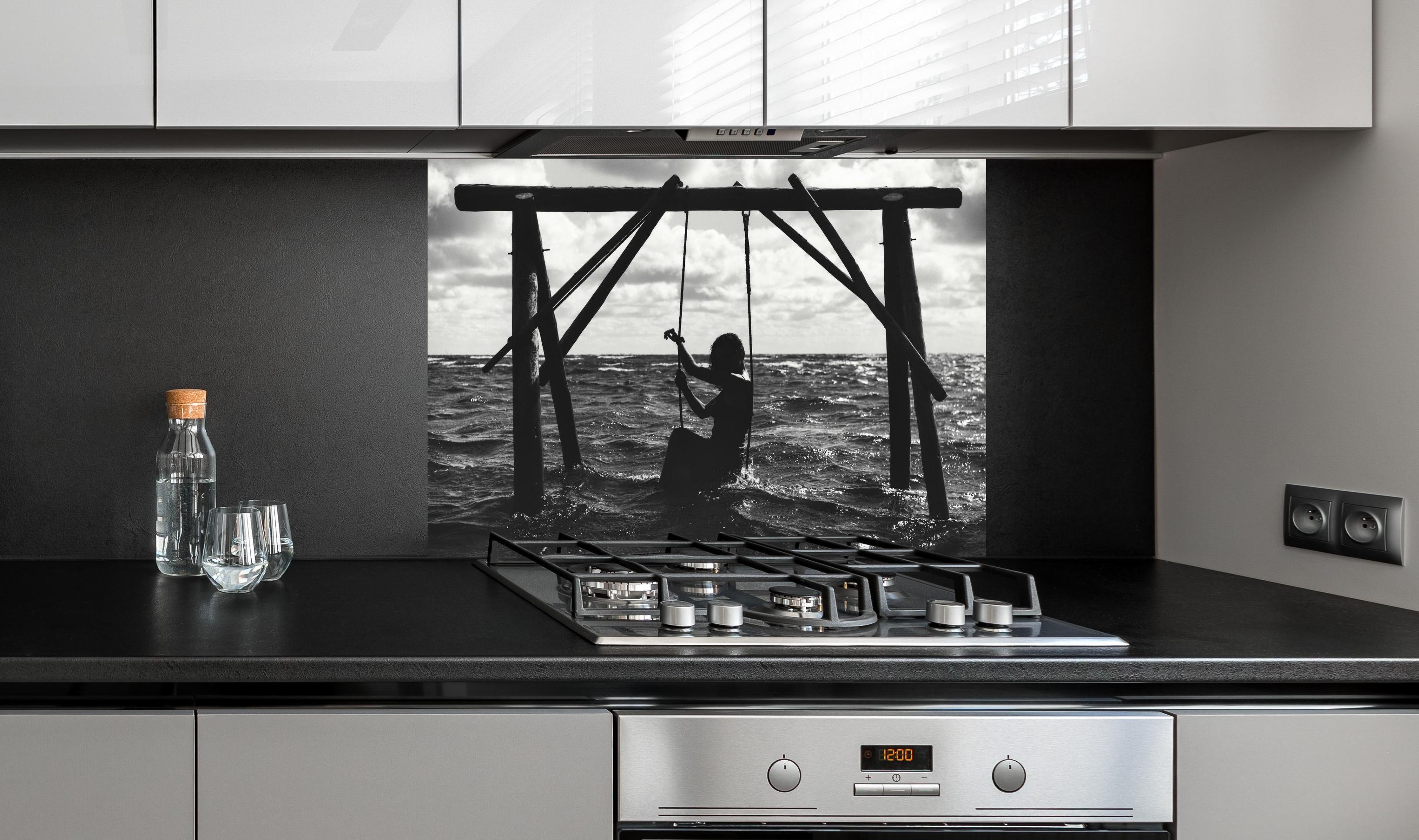 Spritzschutz - Mädchen auf Schaukel im Wasser hinter einem Cerankochfeld zwischen Holz-Kochutensilien