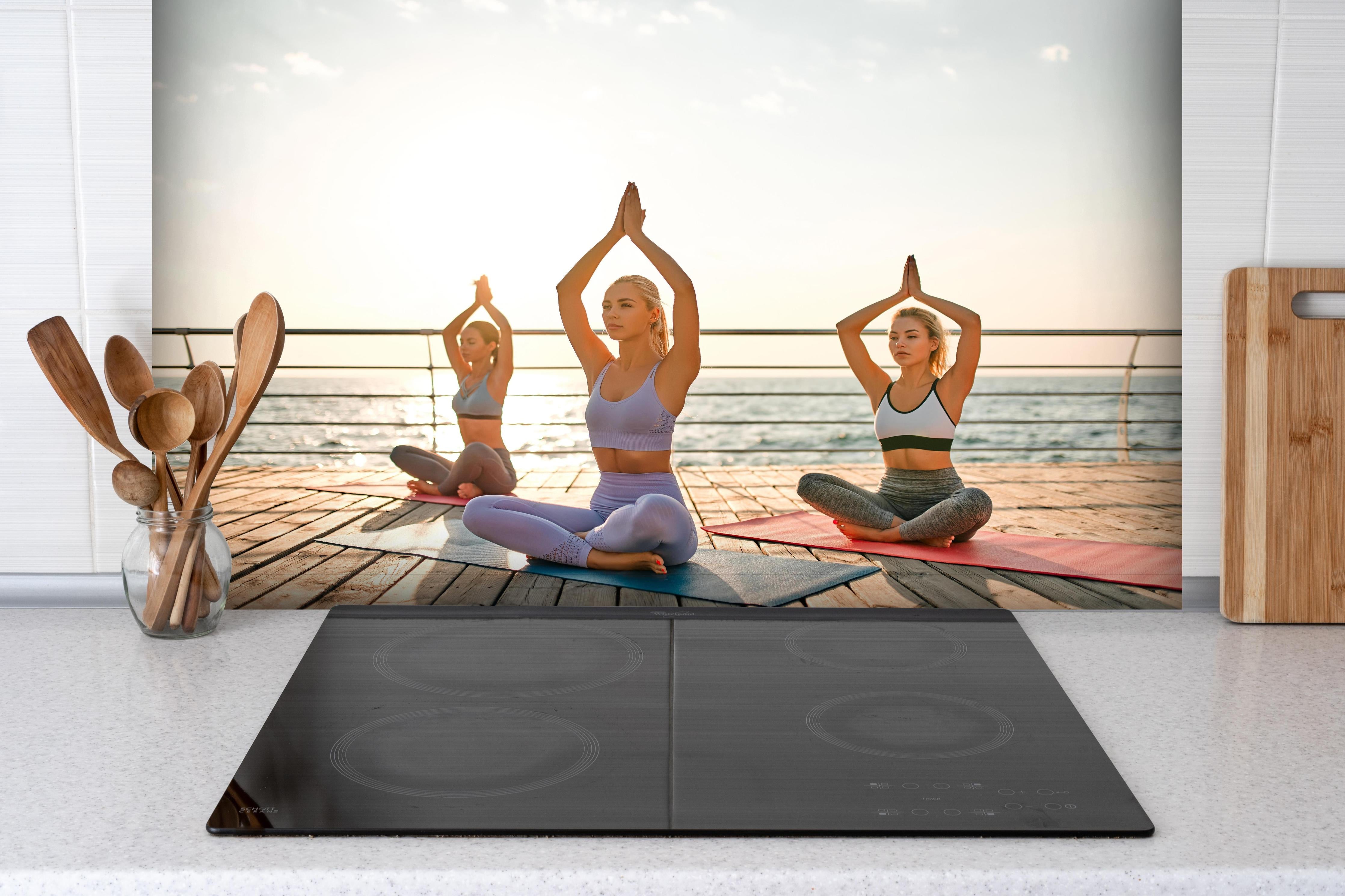 Spritzschutz - Mädchen beim Yoga am Morgen hinter einem Cerankochfeld zwischen Holz-Kochutensilien