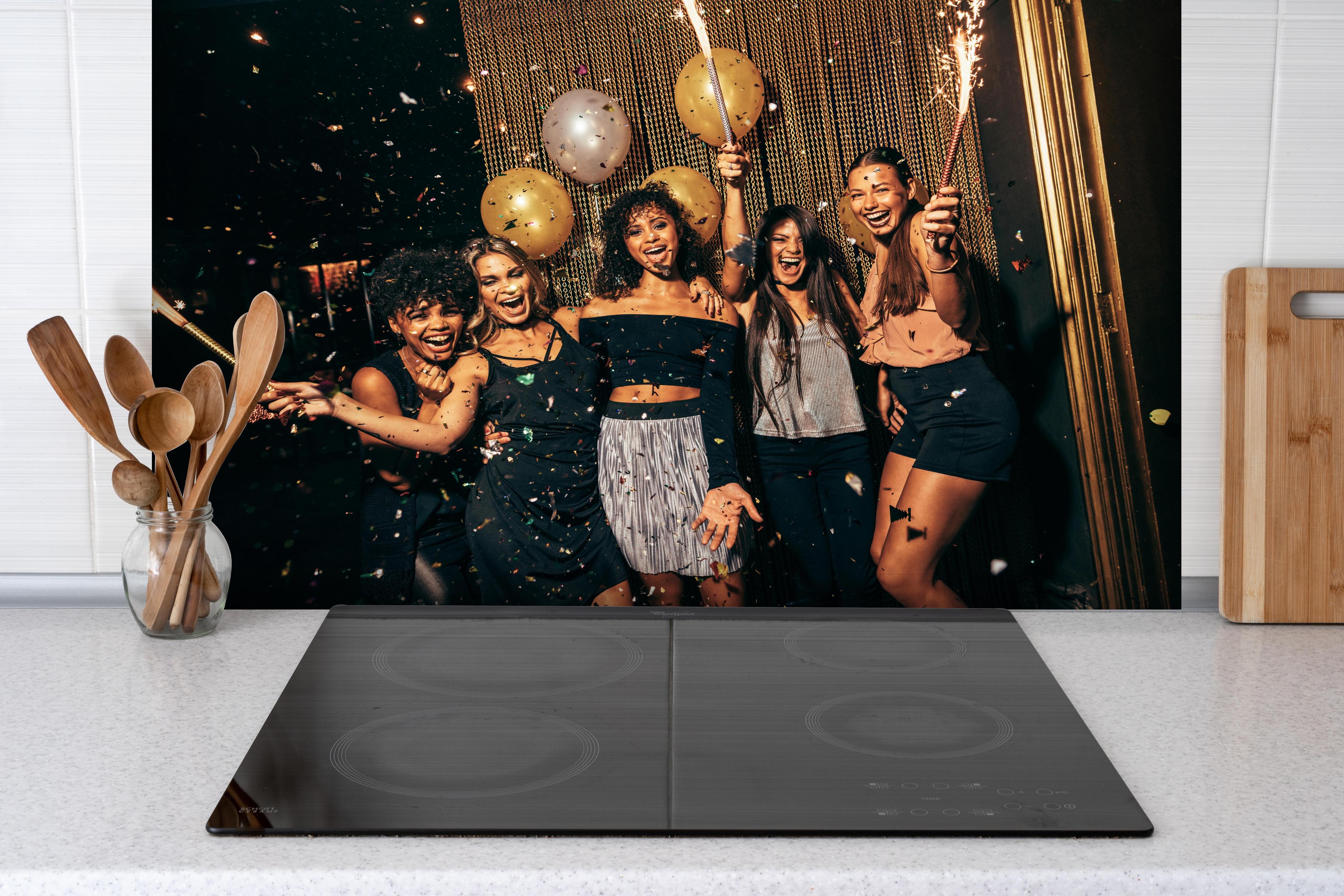 Spritzschutz - Mädchen im Nachtclub haben eine tolle Zeit hinter einem Cerankochfeld zwischen Holz-Kochutensilien