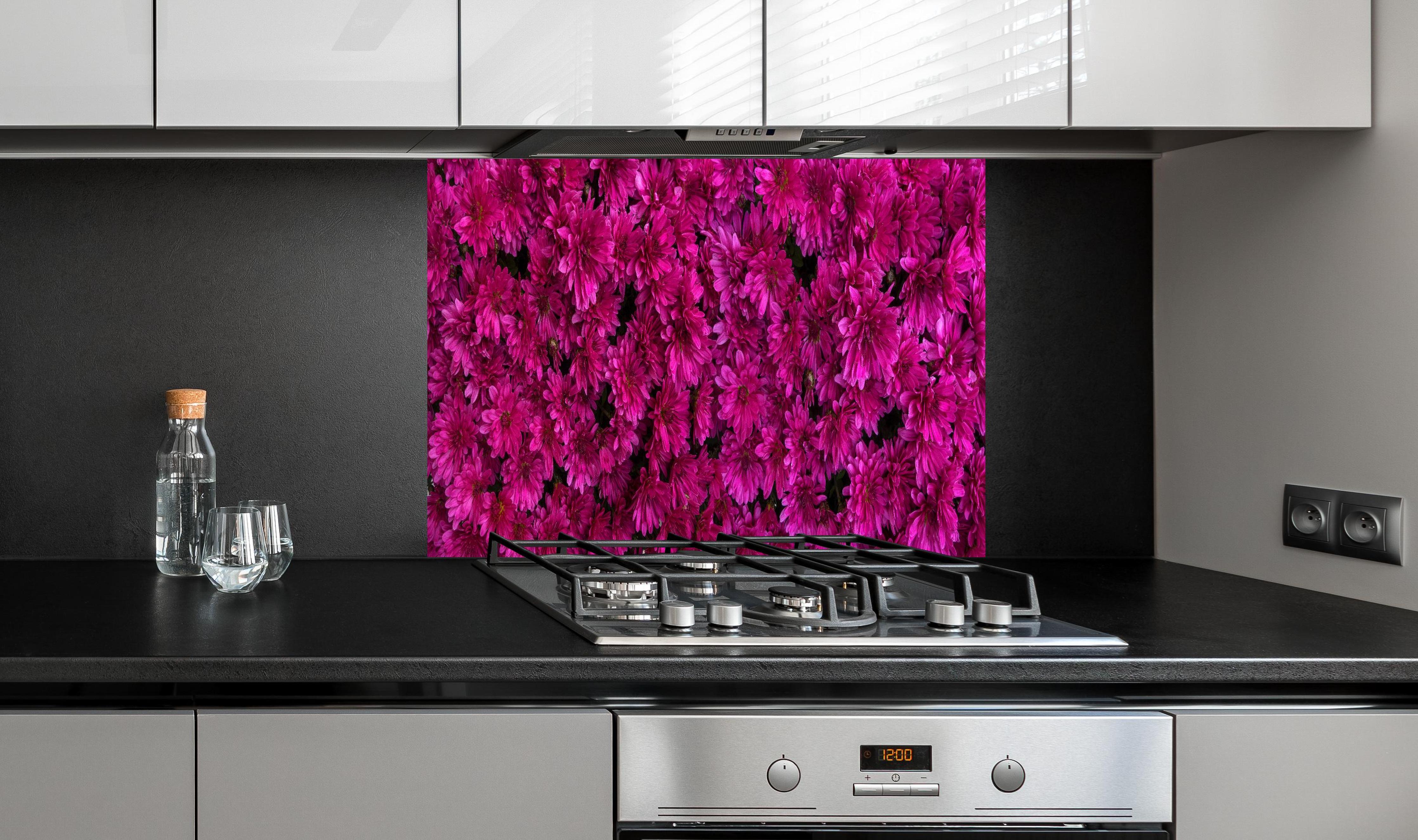 Spritzschutz - Magenta Blüten von Chrysanthemen hinter einem Cerankochfeld zwischen Holz-Kochutensilien